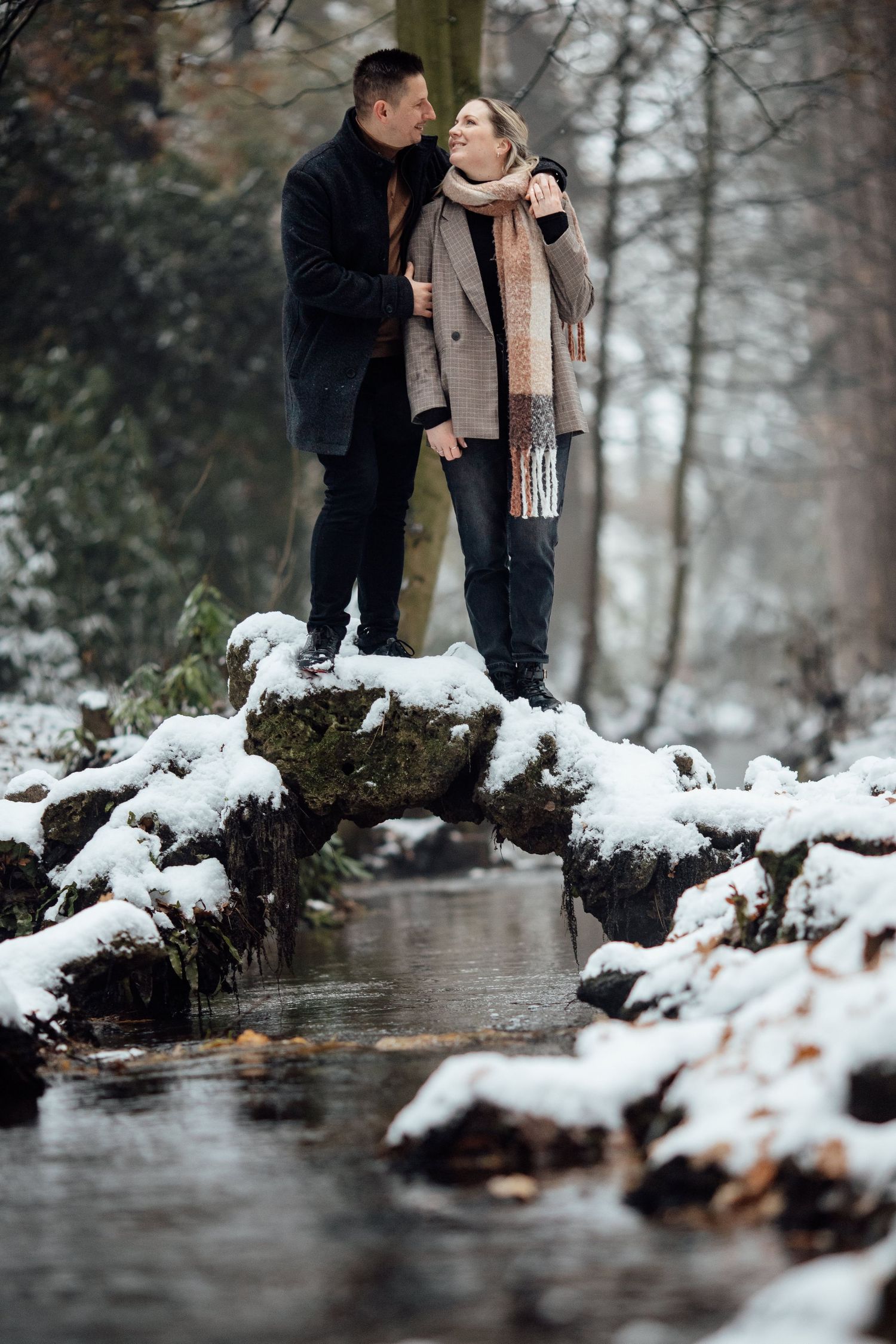 A romantic winter moment captured by a stream with snow-covered rocks and trees.