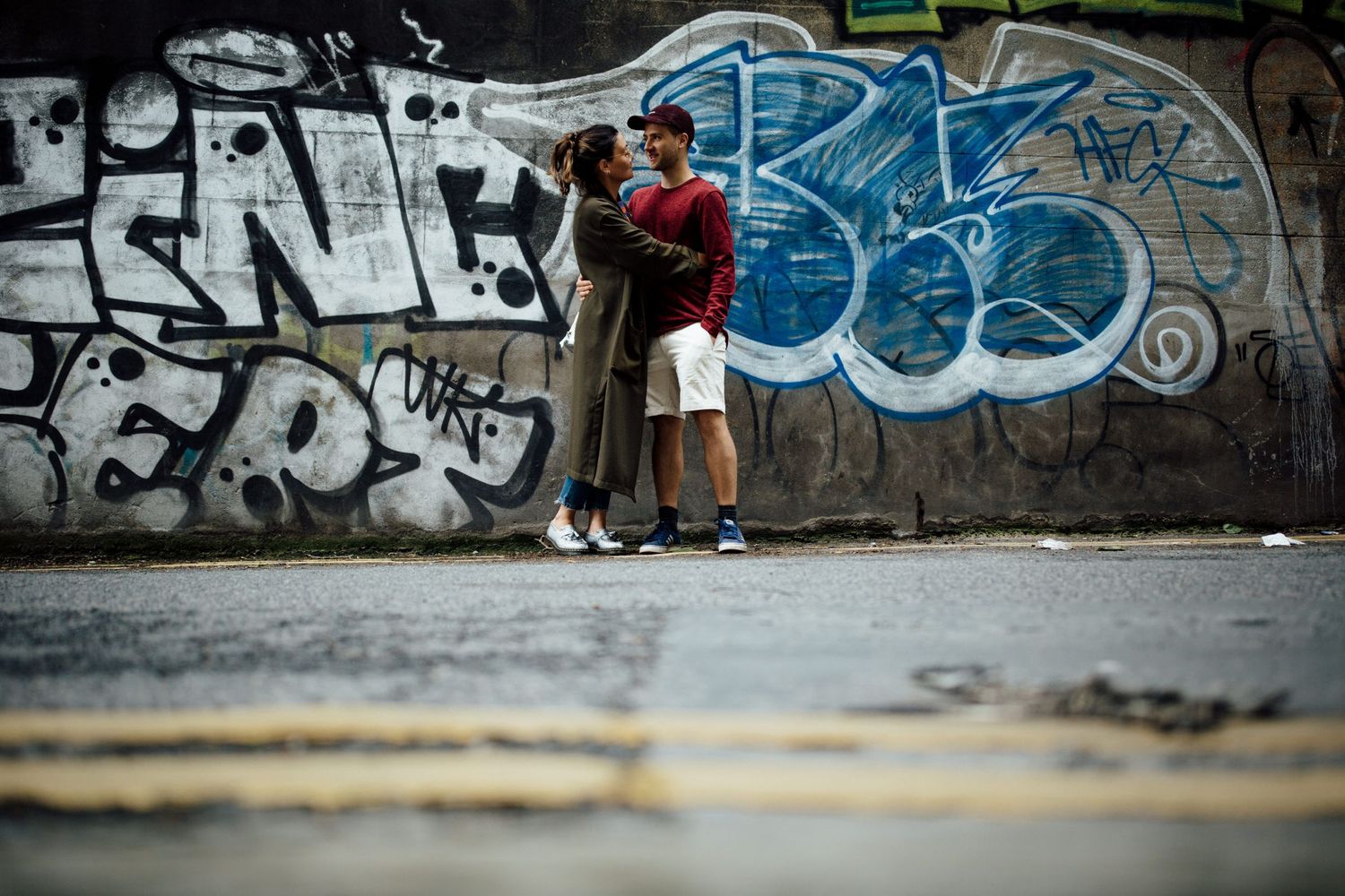 A couple poses against a wall covered in colorful street art and graffiti.