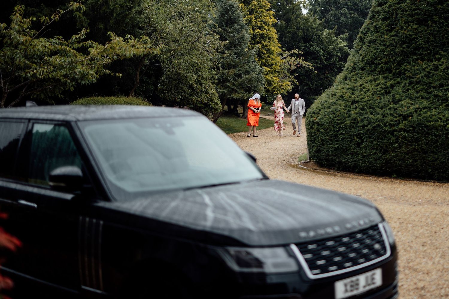 Wedding cars parked along a tree-lined driveway at an elegant venue.
