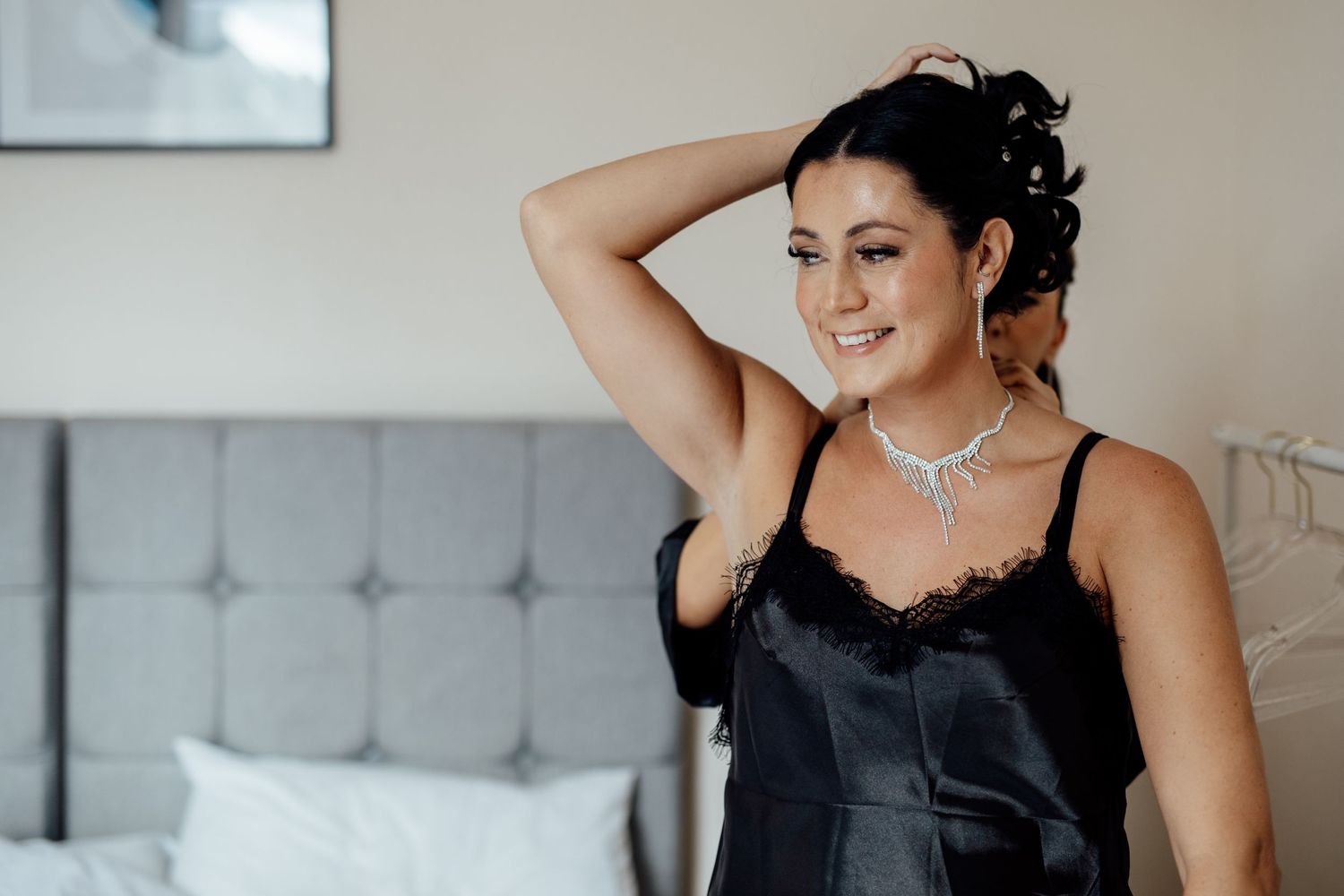 Getting ready moments captured in elegant grey room with tufted headboard.