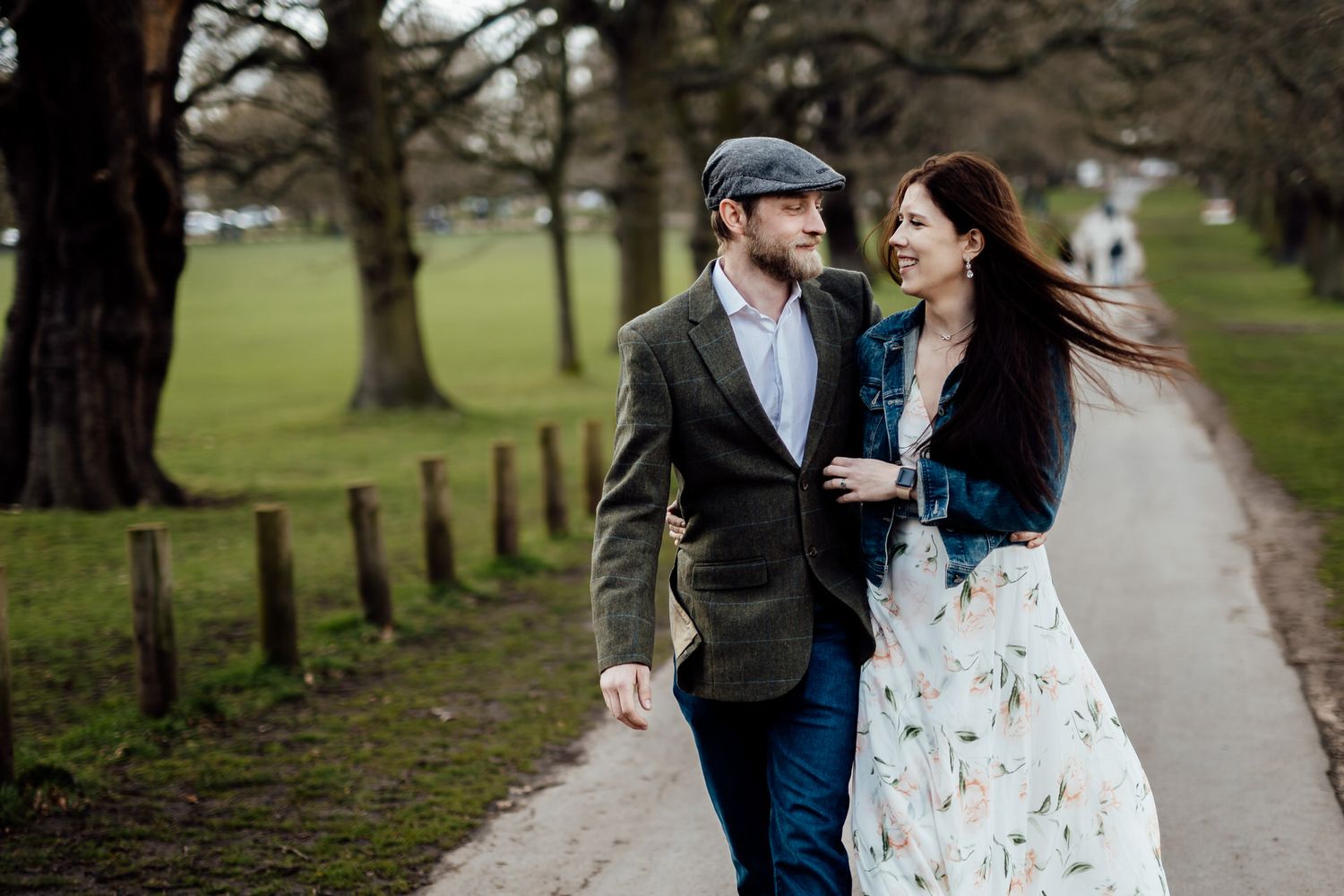 A couple shares a laughing moment while walking on a path surrounded by trees.