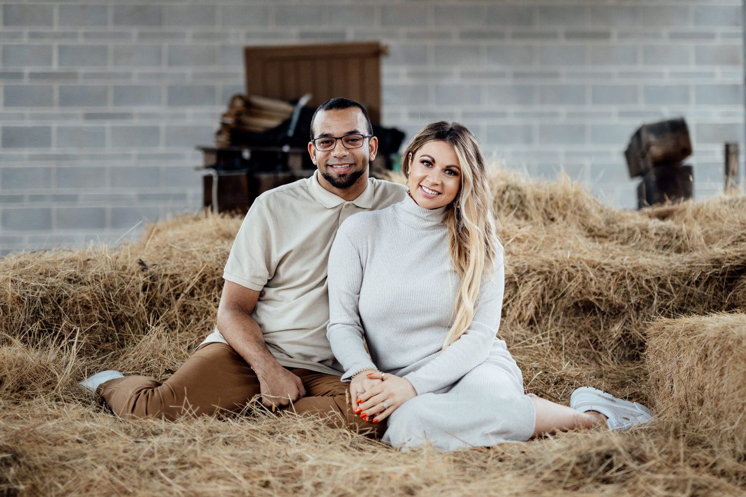 A couple relaxes together on hay bales during a rustic outdoor photoshoot.