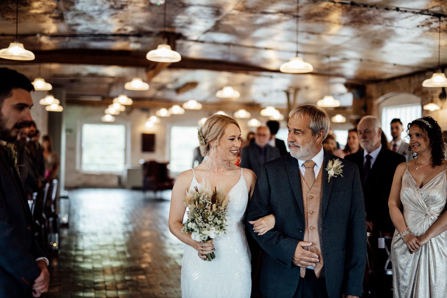 Wedding guests enjoying a celebration in a rustic indoor venue with exposed brick walls and pendant lighting.