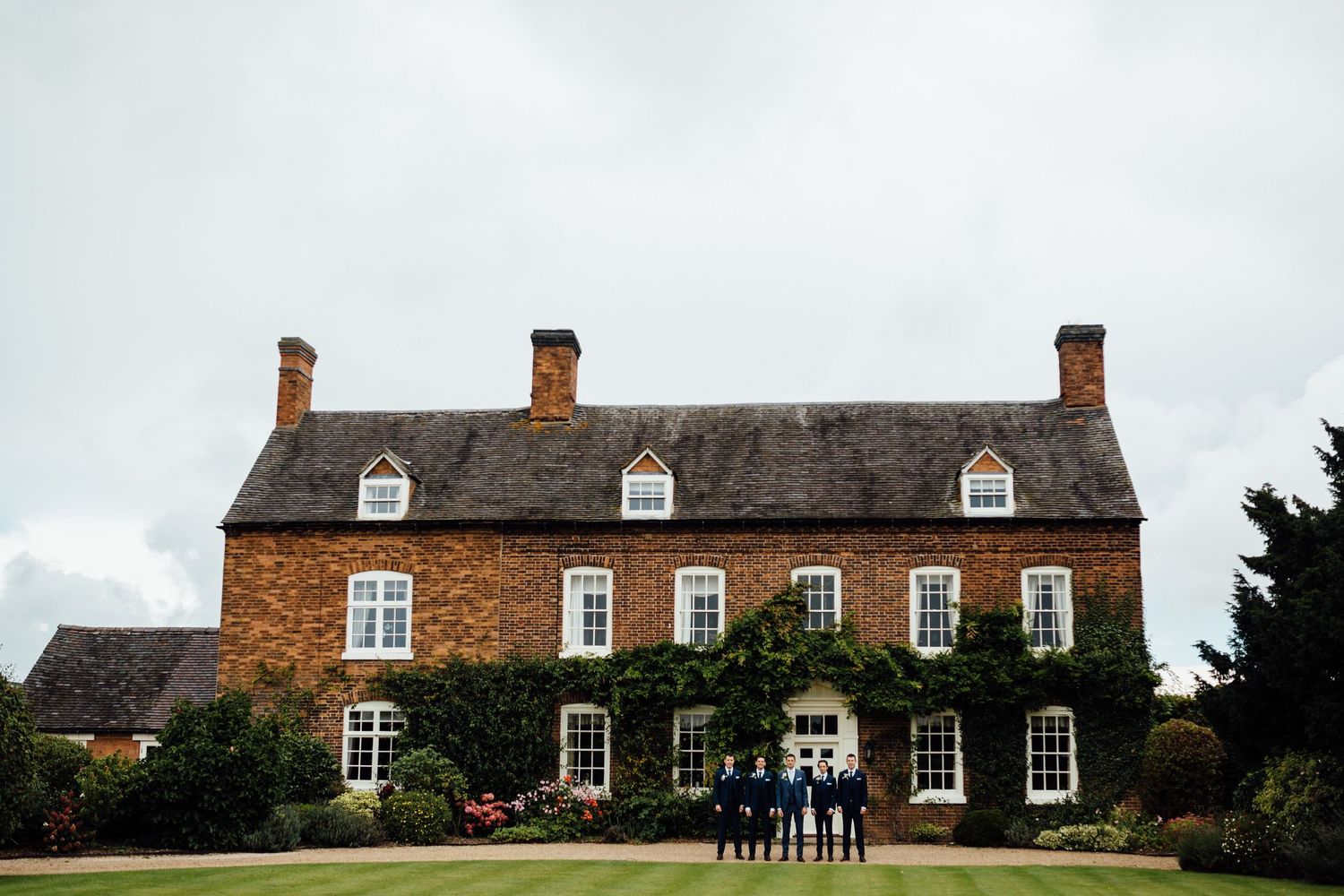 Panoramic view of a traditional English brick farmhouse with multiple buildings on a cloudy day.