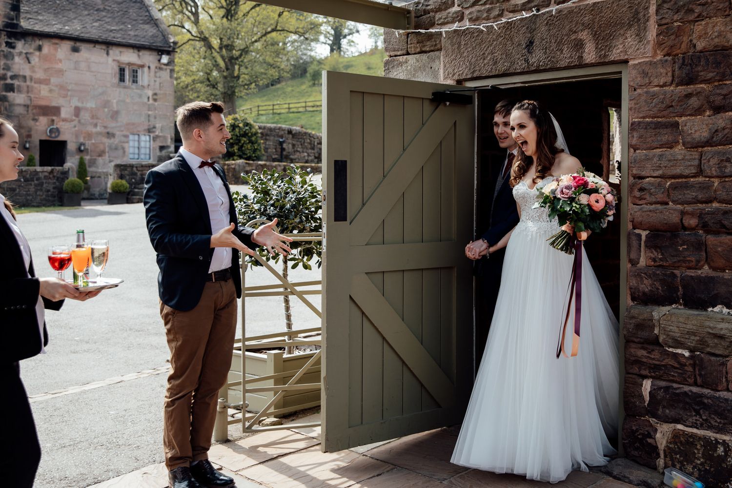 Wedding party gathered outside rustic stone building with green wooden door.