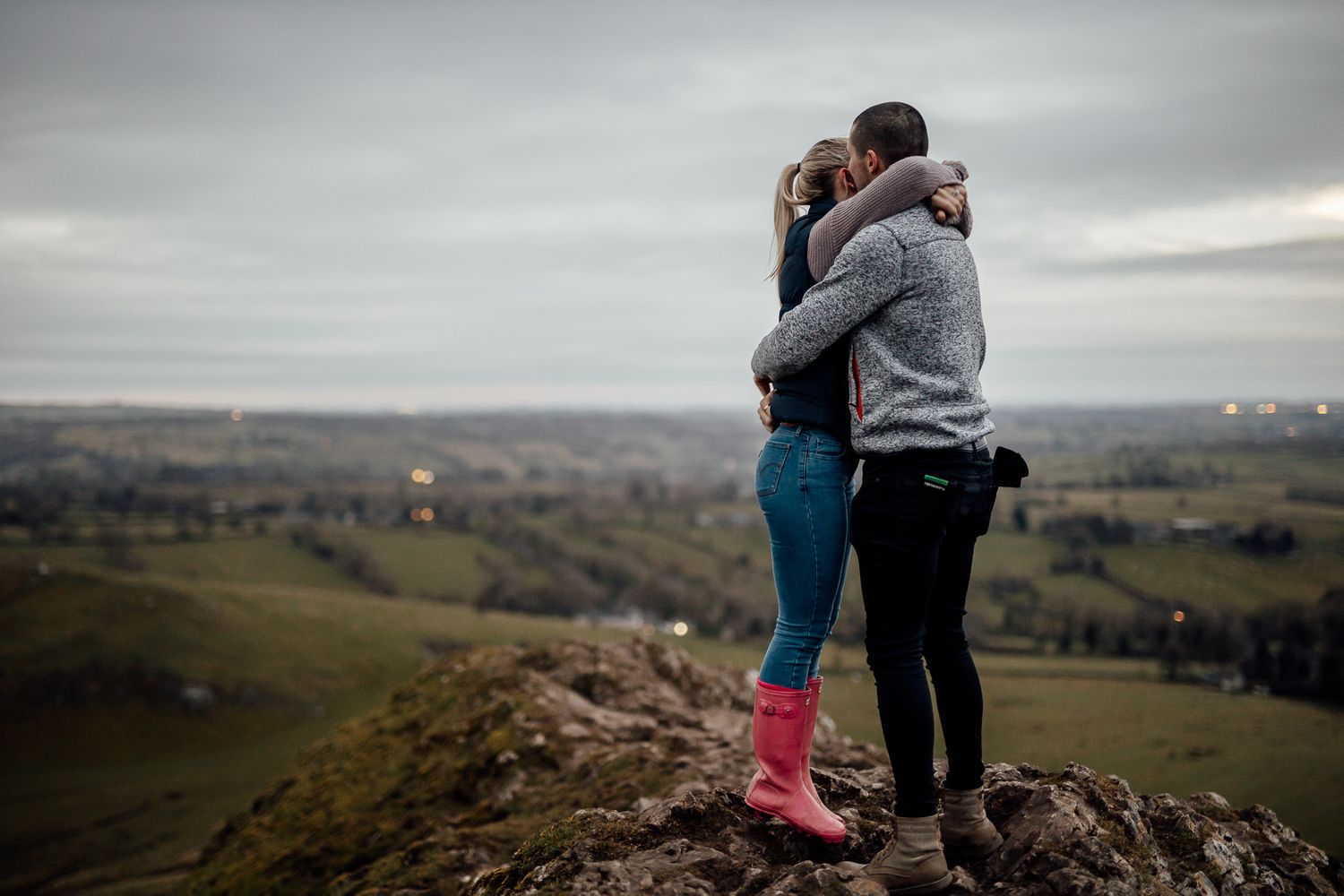 A couple stands together on a hilltop with pink boots adding a pop of color to the scene.