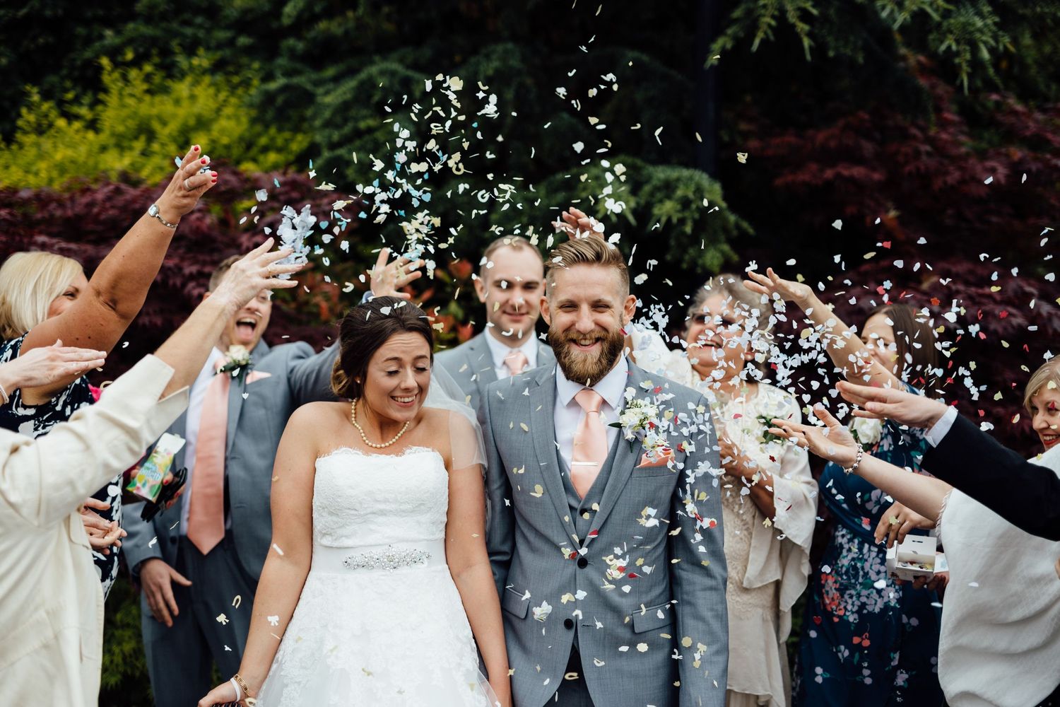 Wedding party celebrating outdoors with confetti and joyful expressions.