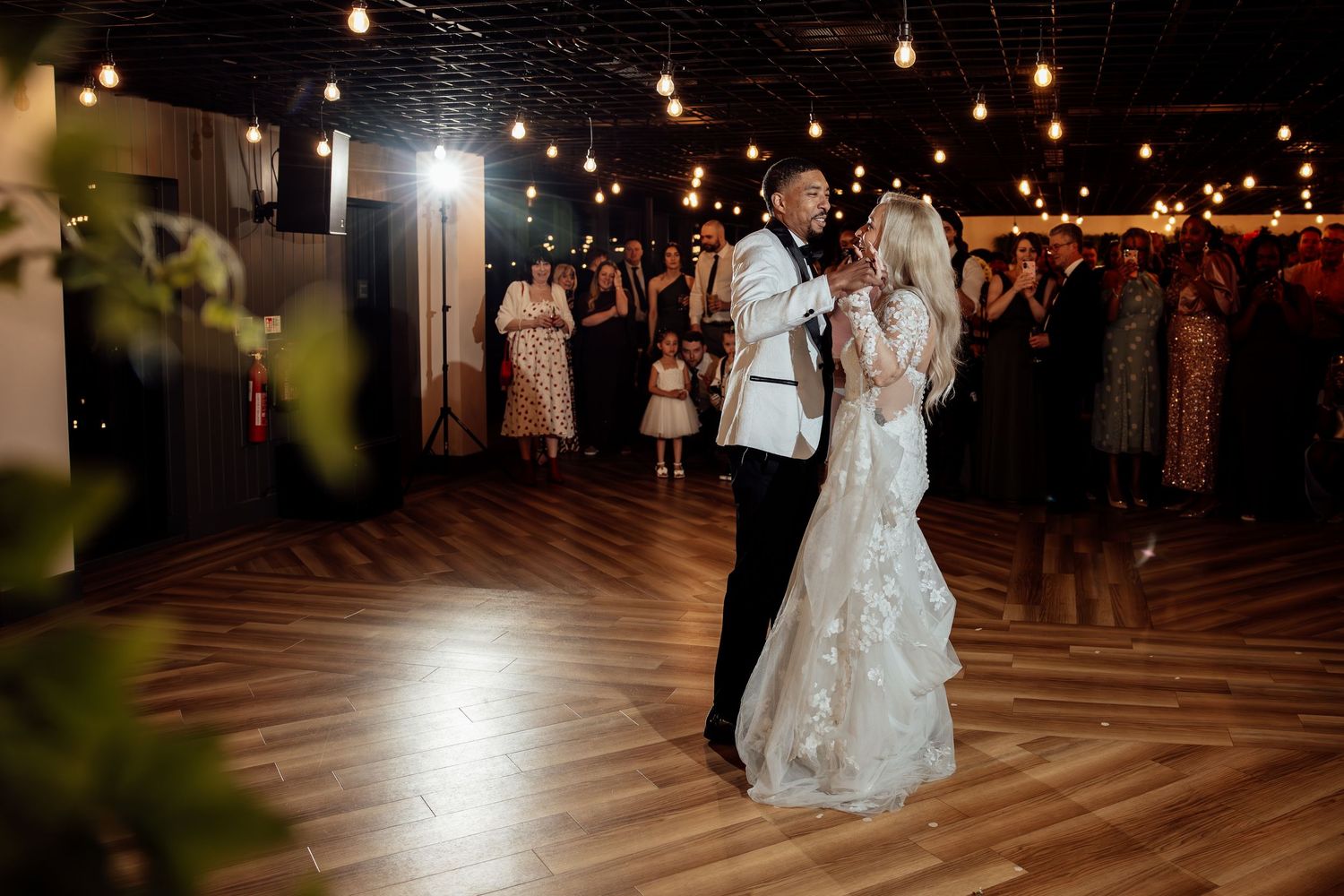 Bride and groom share first dance under warm string lights at wedding reception.