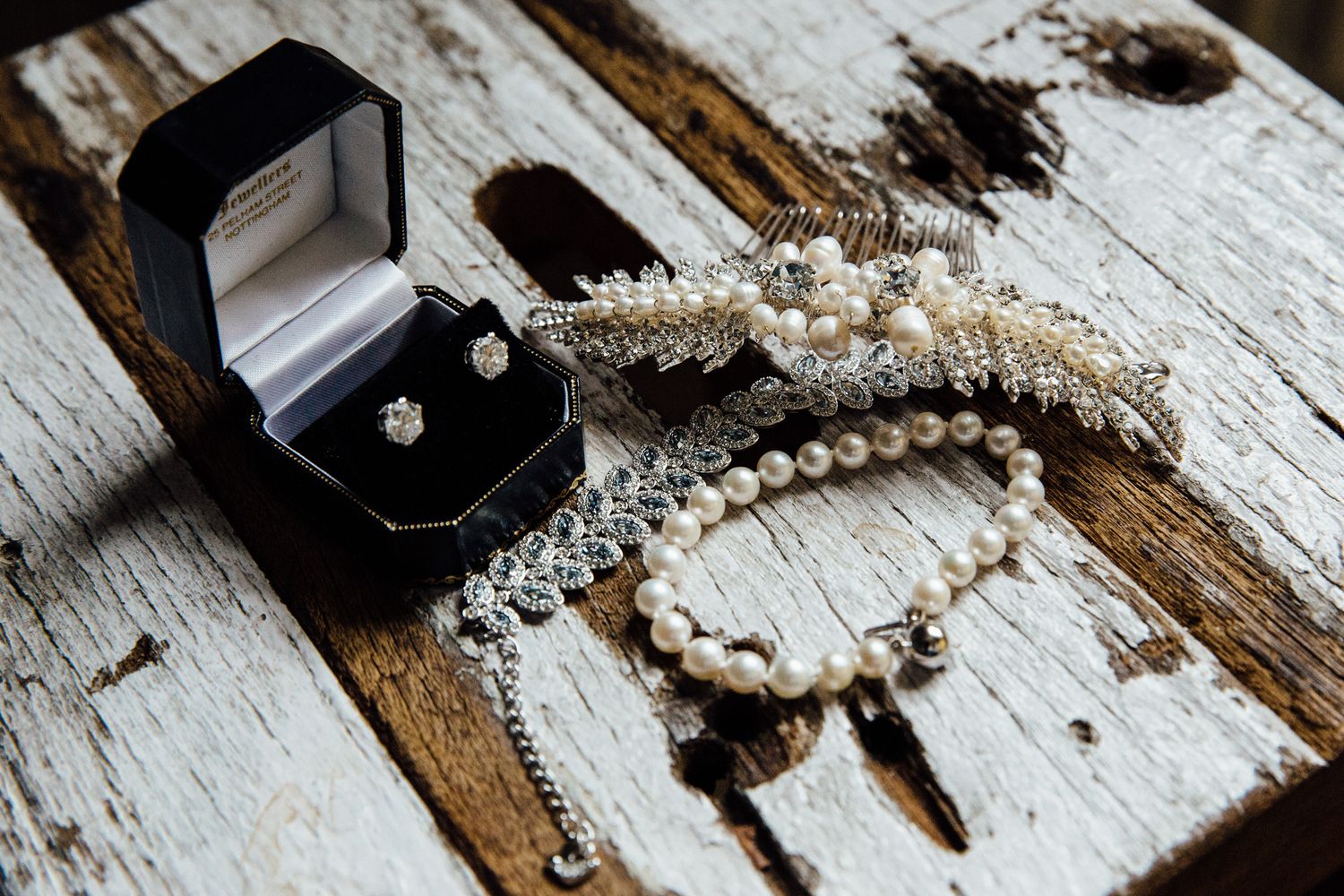 Wedding rings and pearl jewelry arranged on rustic white wooden surface for detail shots.