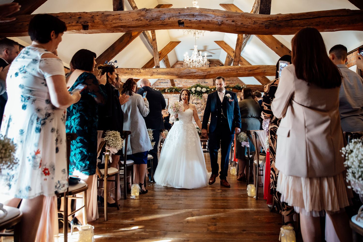 Wedding guests dancing and celebrating on a rustic wooden dance floor under exposed beams.