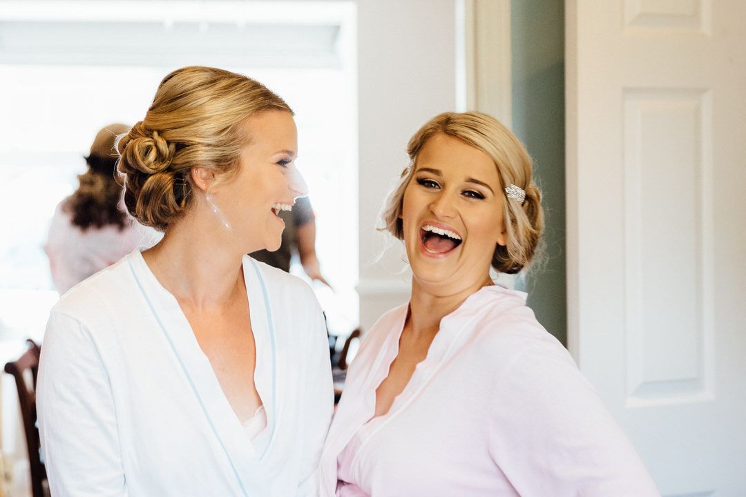 Bridesmaids in white robes gather during wedding morning preparations.