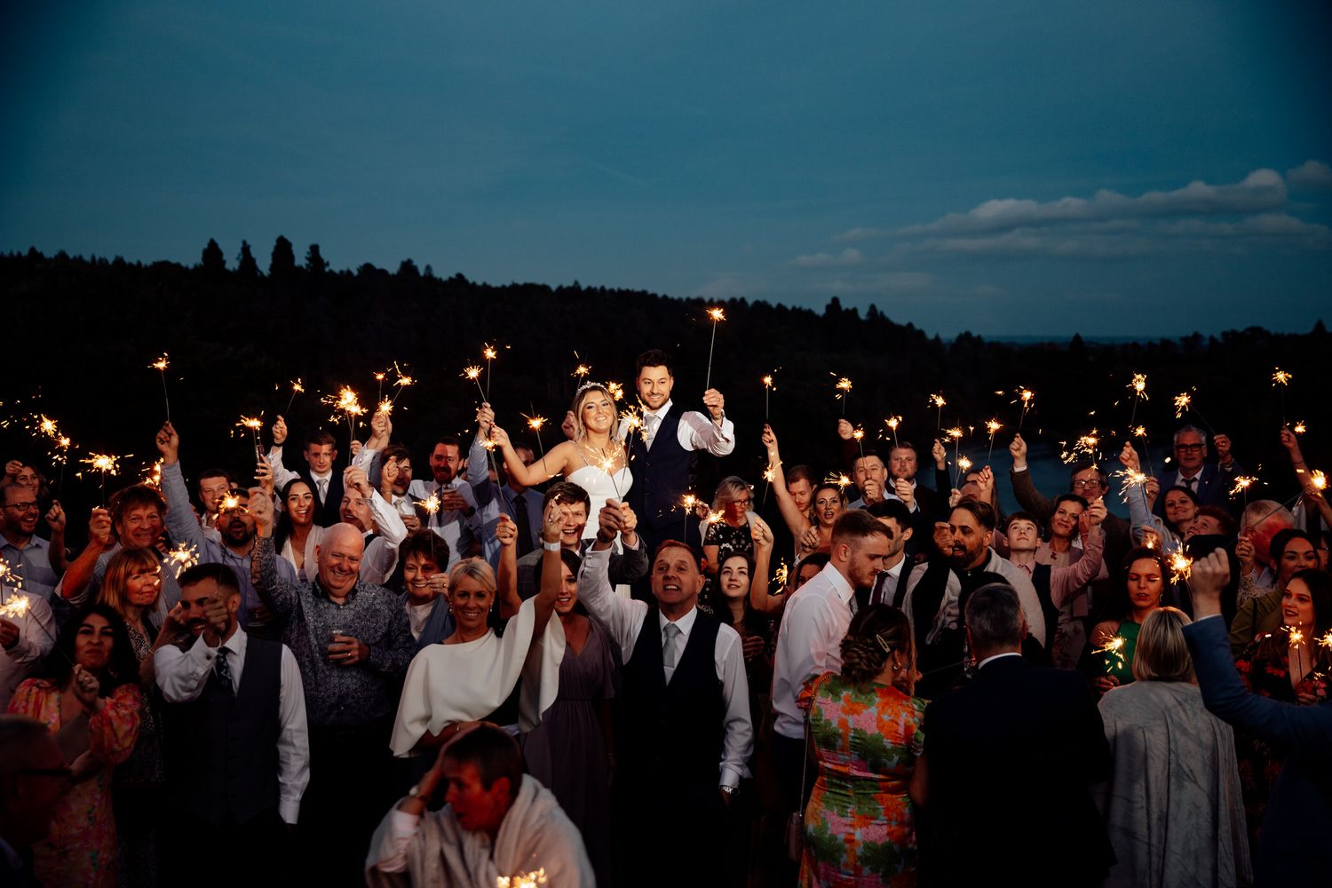 Large crowd holding sparklers at nighttime outdoor wedding celebration.