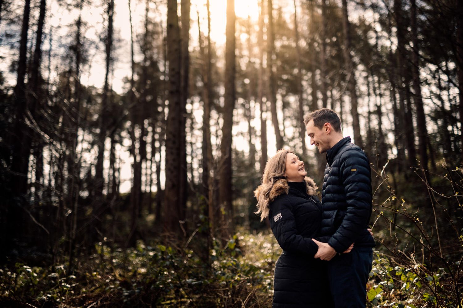 Couple embracing and laughing together in a sunlit pine forest.