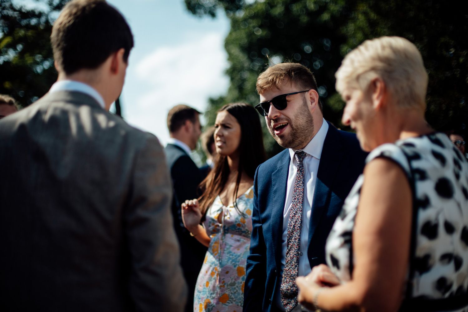 Wedding guests mingle outdoors during a sunny daytime reception.