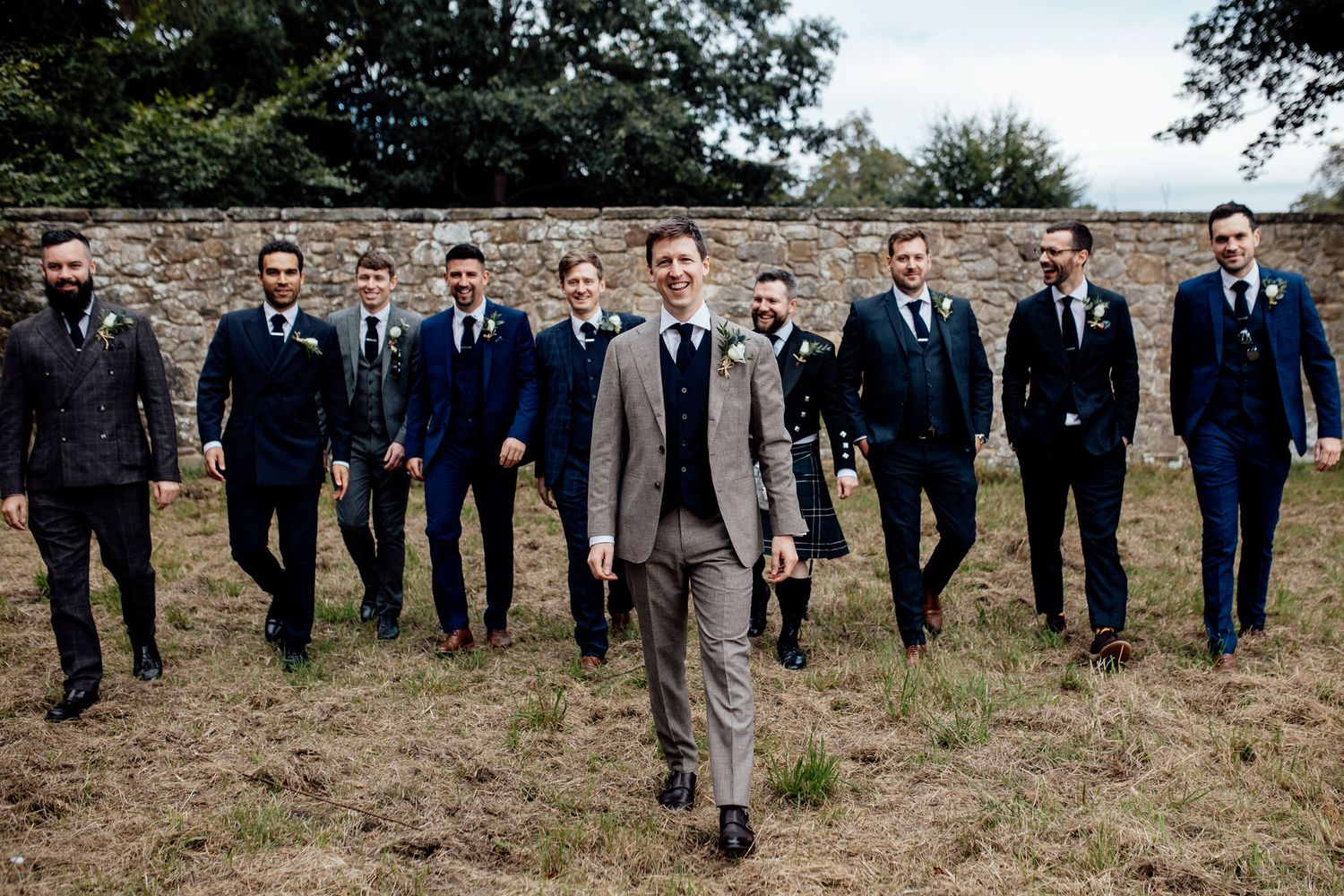 Groomsmen in dark suits posing together outdoors in a rustic field setting.