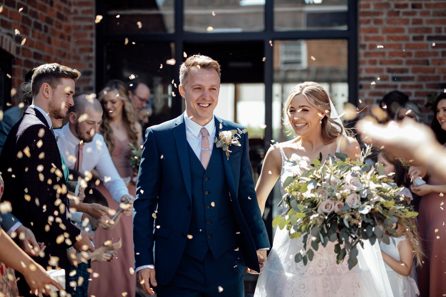 Wedding celebration outside brick building with confetti floating in the air.