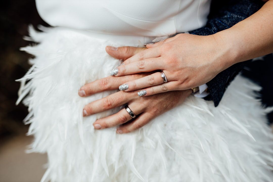Close-up of hands showing wedding rings against a white feathered dress.