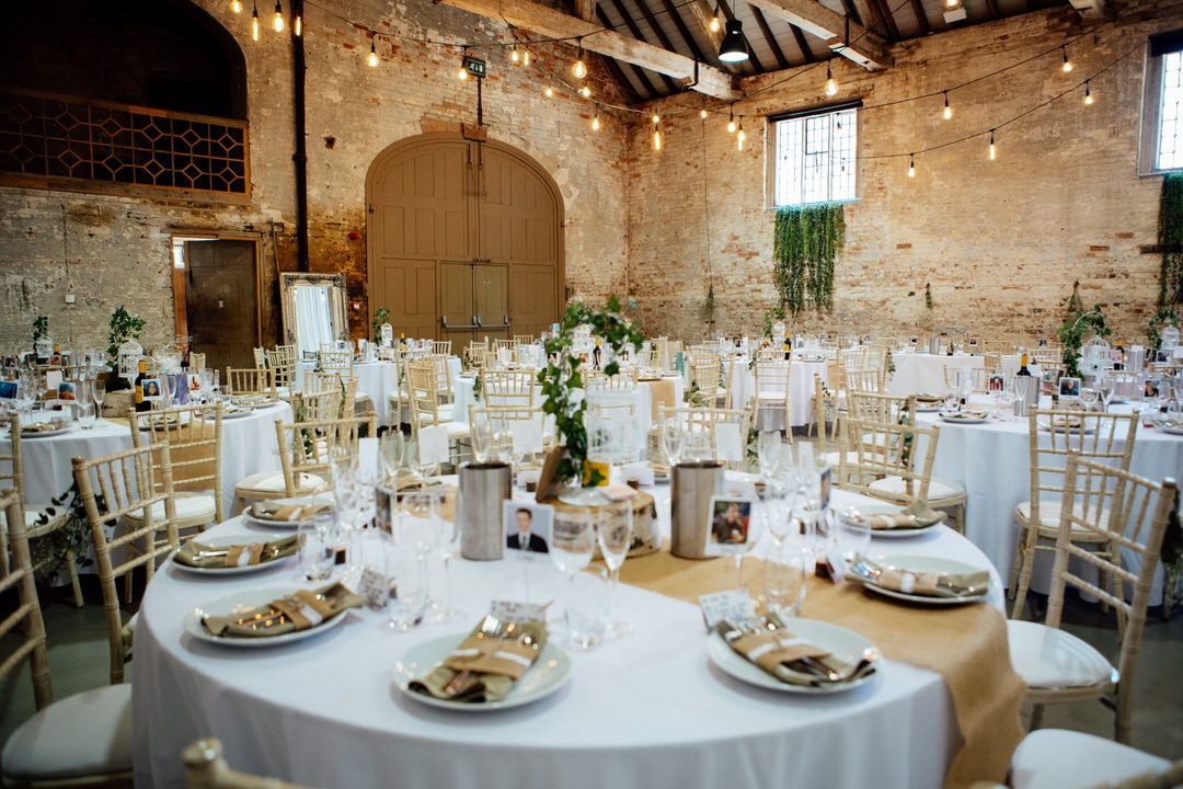 Elegant wedding reception venue with exposed brick walls, string lights, and white table settings.