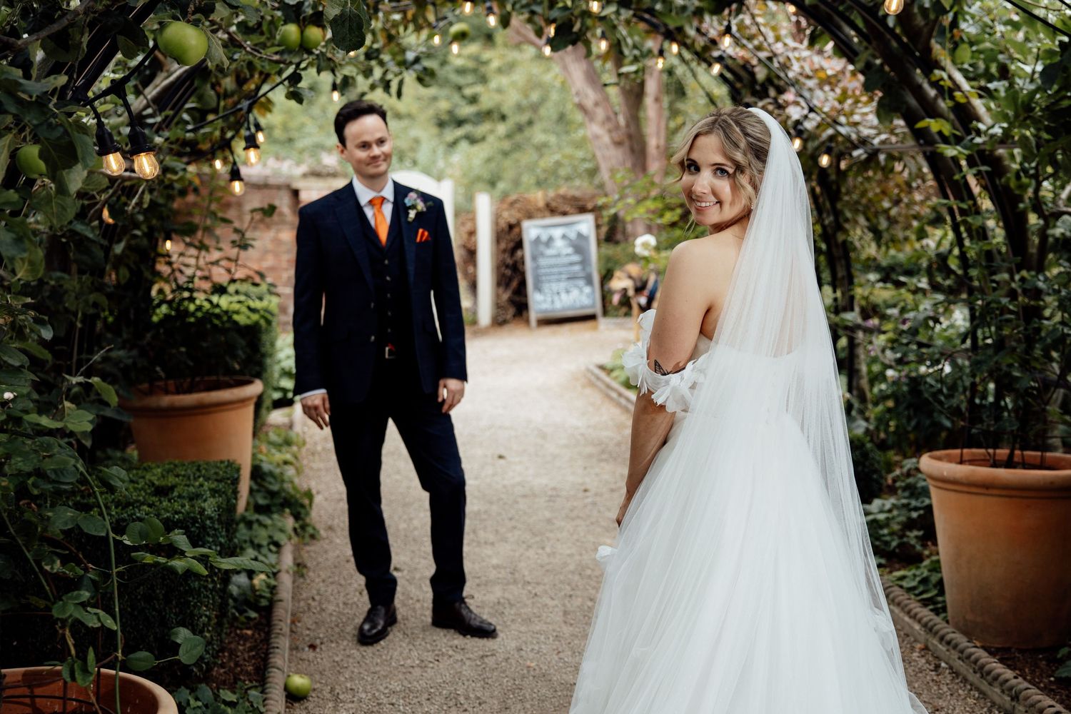 Romantic garden wedding portrait with couple posing along potted plant lined pathway.