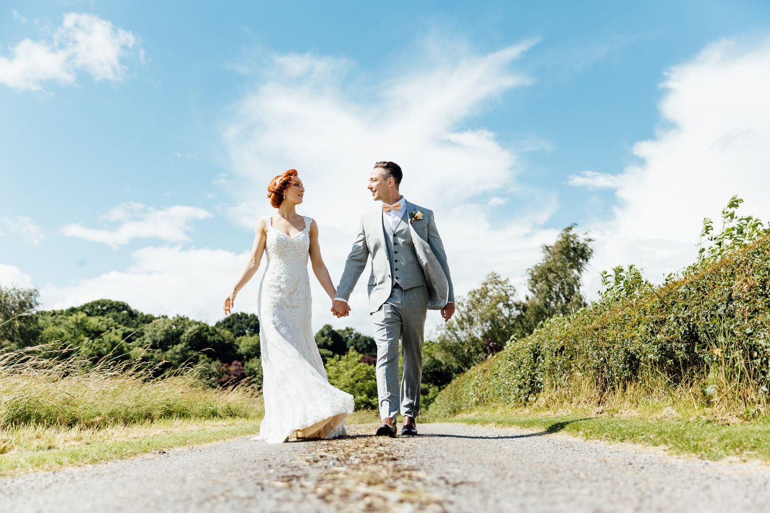 A couple walking hand in hand down a country path on their wedding day.