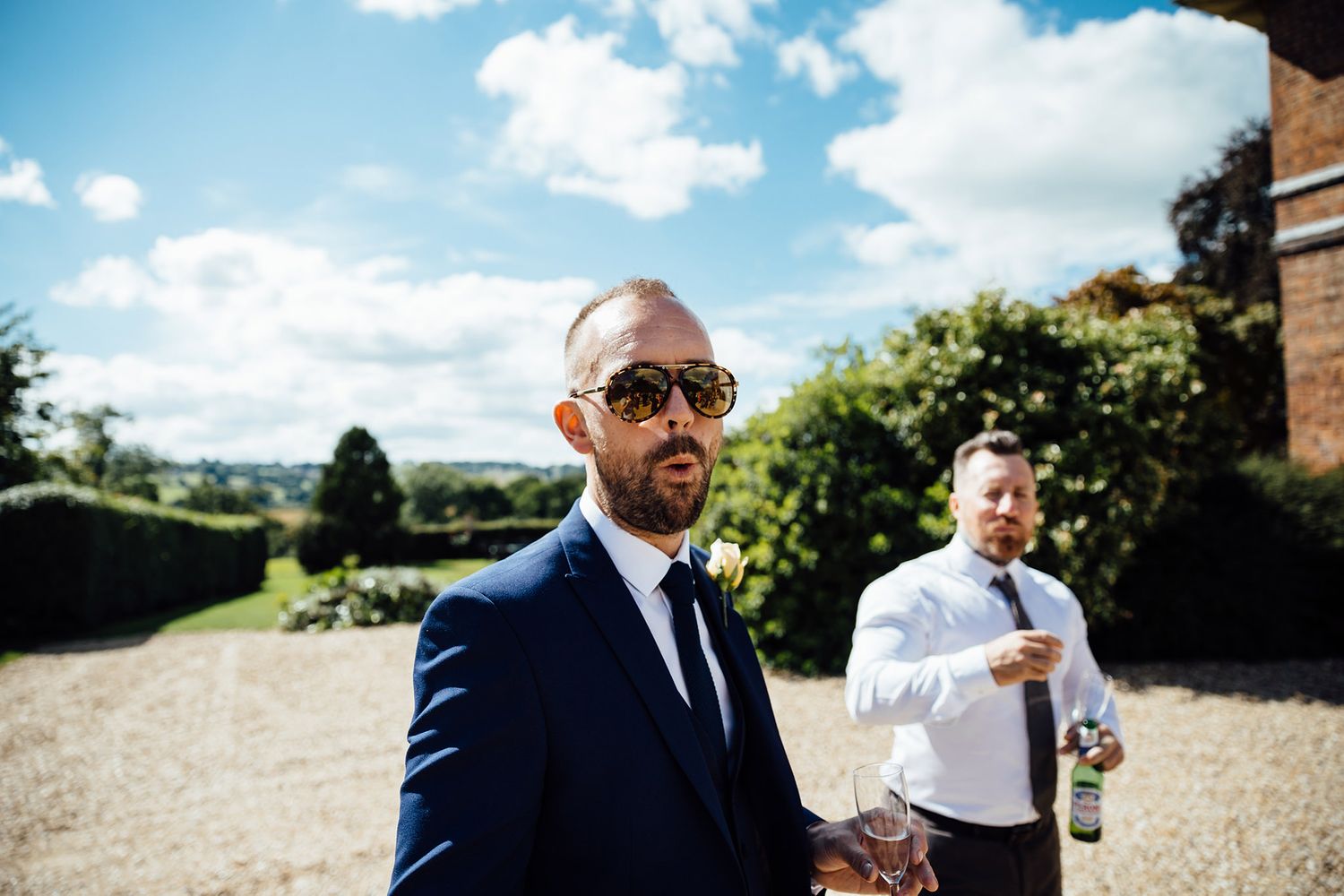 Wedding party members enjoy drinks outdoors on a sunny day with blue skies.