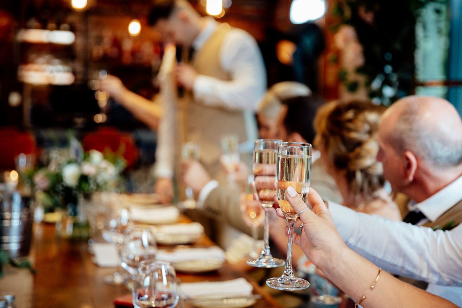 Wedding reception dinner tables set with wine glasses and ambient lighting in a rustic venue.