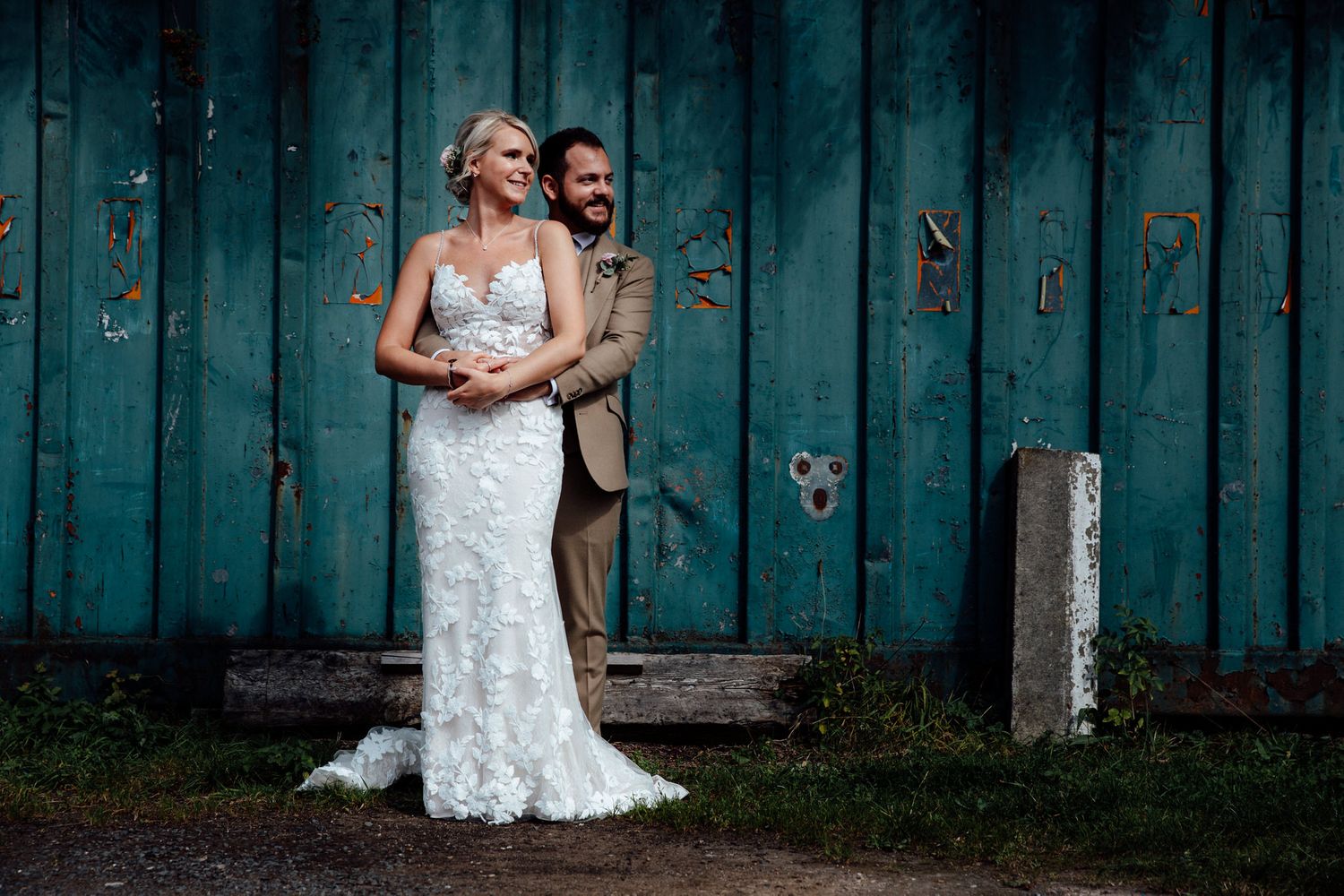 Couple in wedding attire posing against a rustic blue wooden wall backdrop.