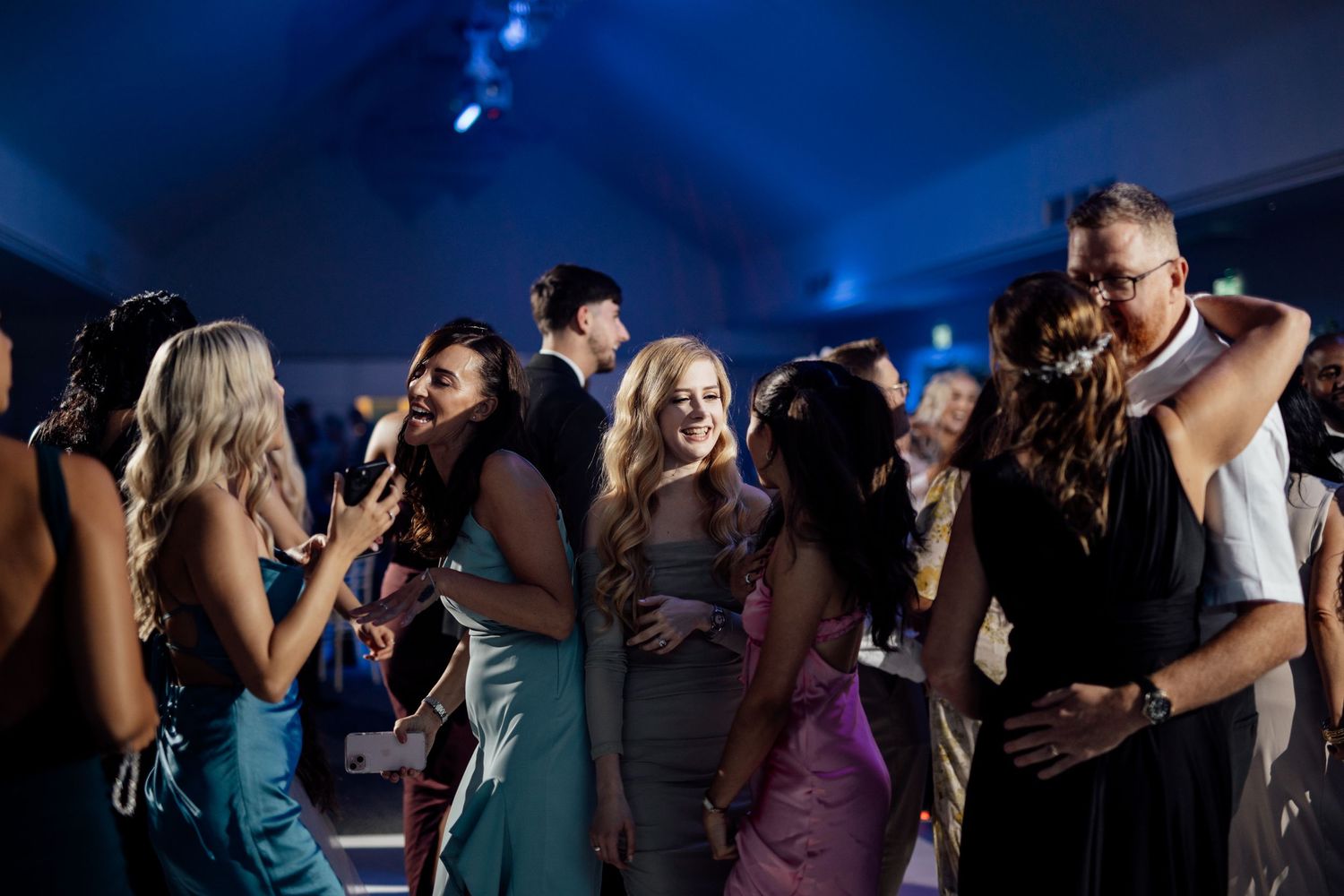 Silhouettes of people dancing at a wedding reception with blue lighting.