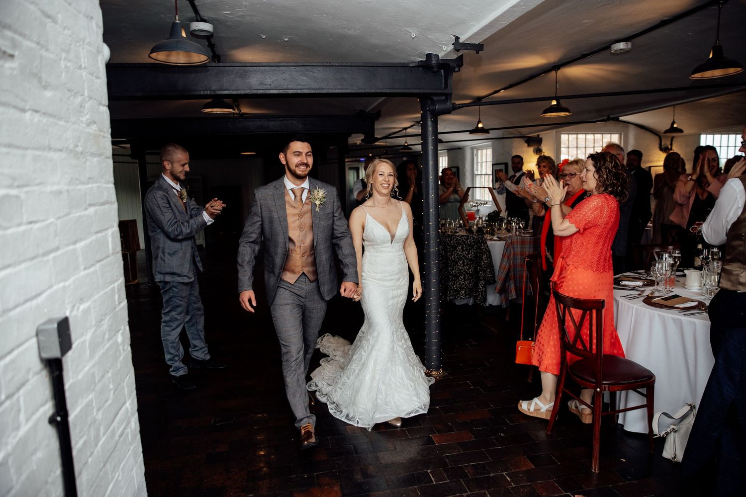 Wedding reception venue with white brick walls and dancing guests in evening lighting.
