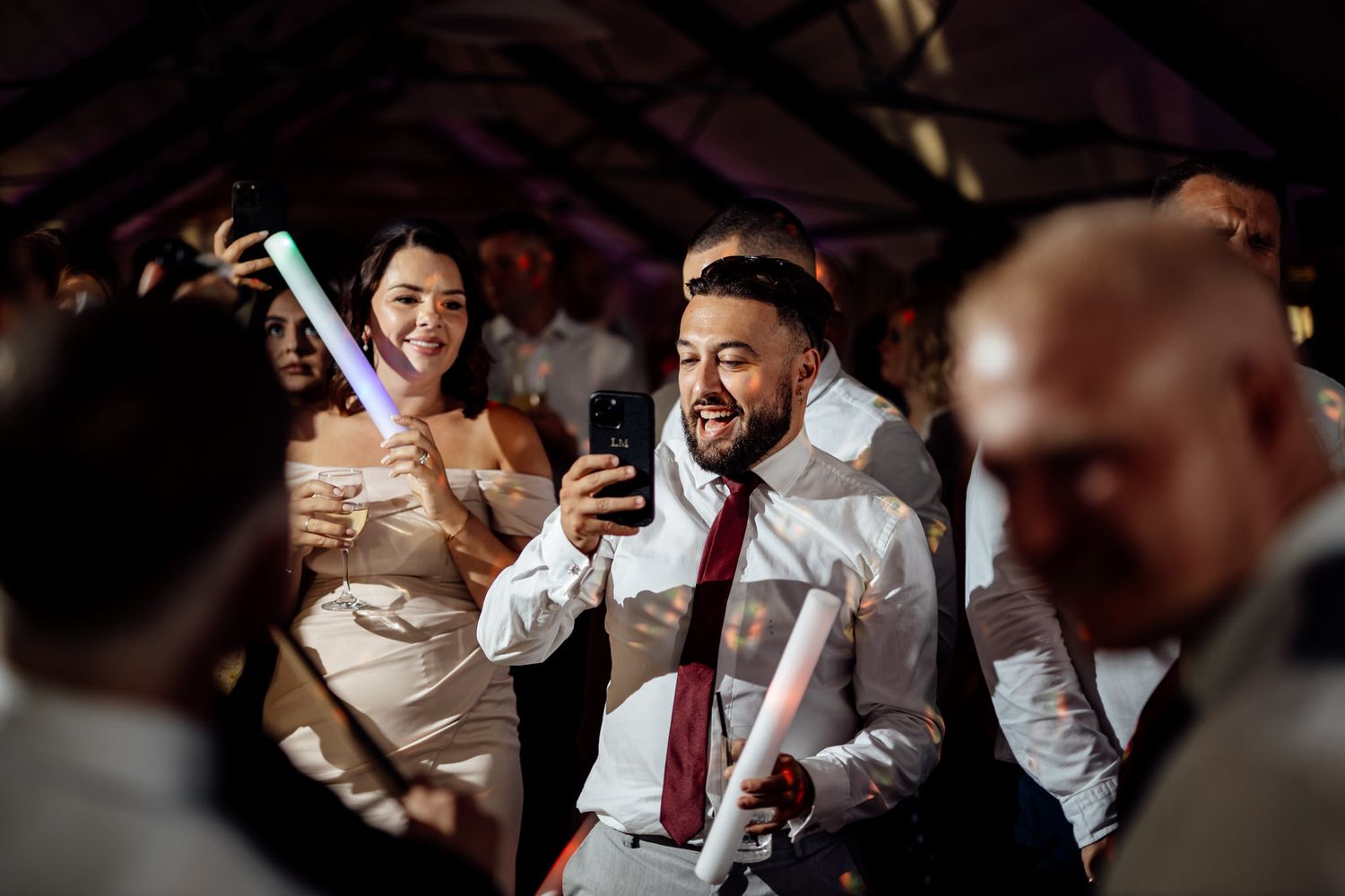 Wedding guests laughing and celebrating during a reception in a dark venue.