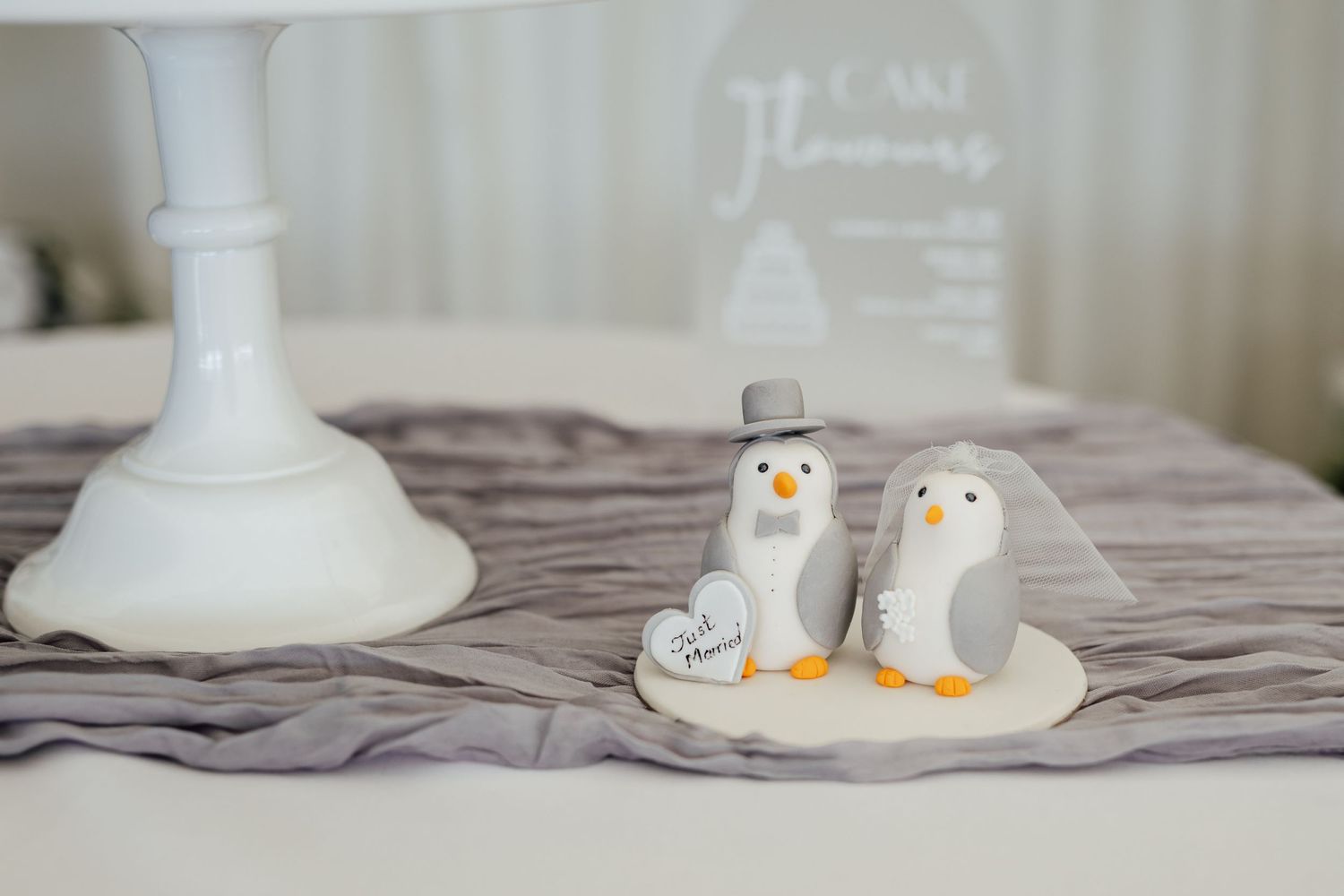 Two cute penguin cake toppers displayed on a table with white decor.