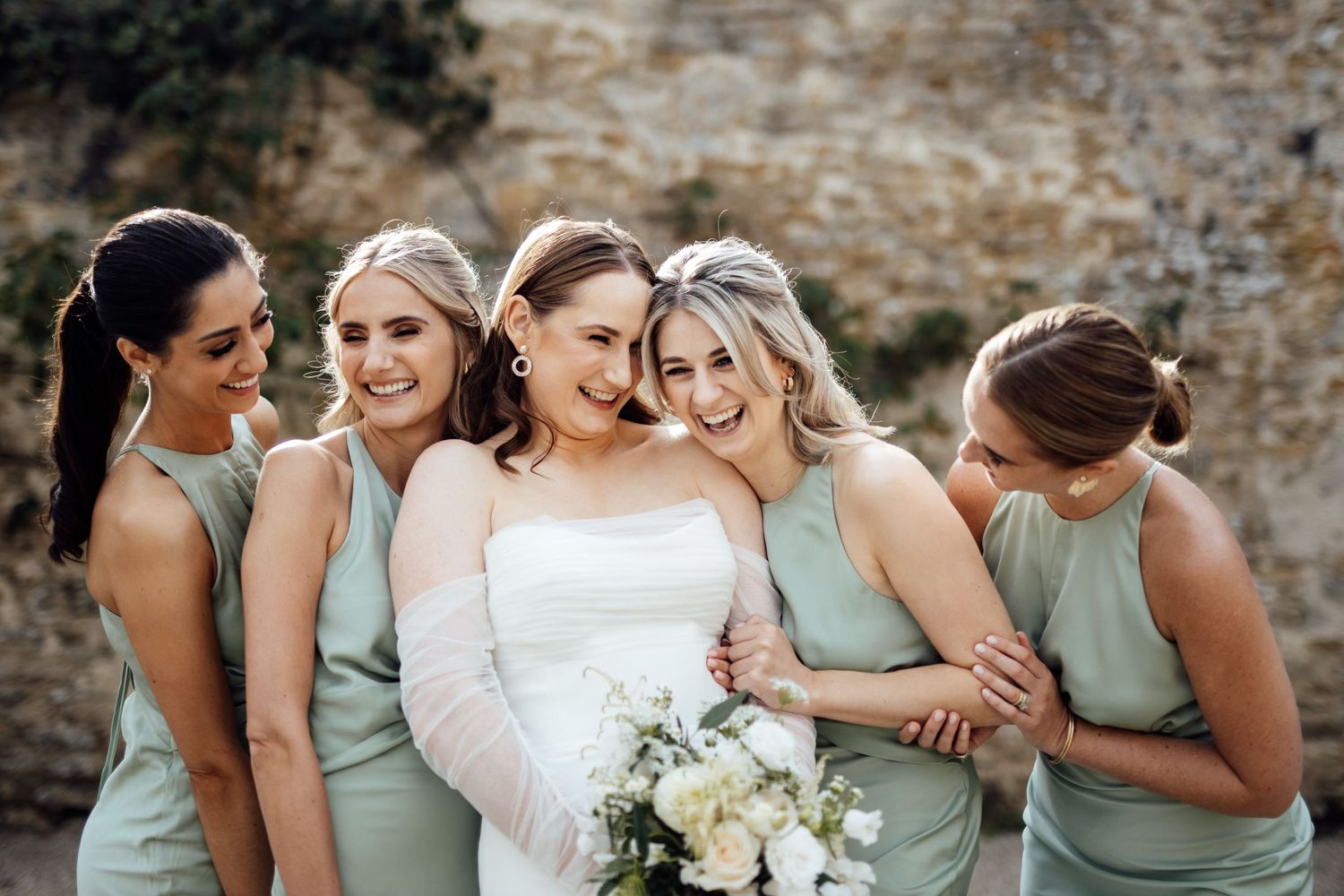 Bridesmaids in sage green dresses share joyful moments during wedding photoshoot.