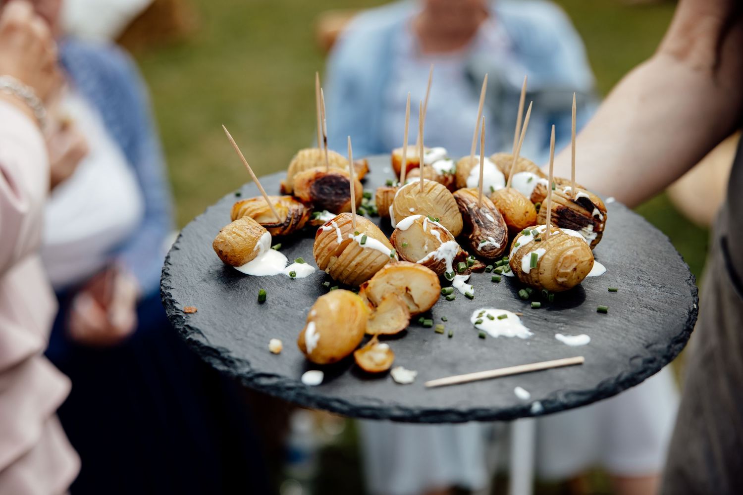 Appetizers served on a slate platter with toothpicks at an outdoor event.