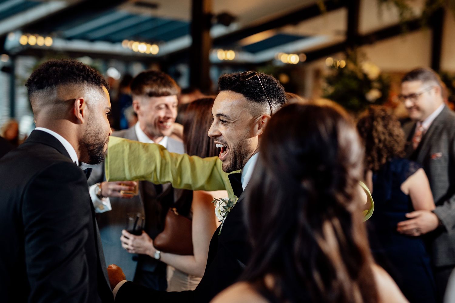 Wedding reception guests celebrate and dance in a dimly lit indoor venue.