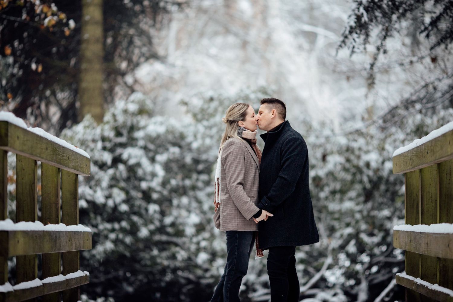 Couple embracing in front of a snowy brick wall during an intimate winter photoshoot.