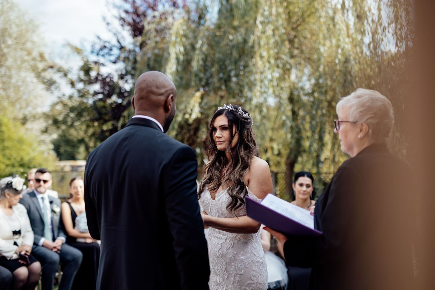 Wedding ceremony guests gather outdoors under natural lighting.