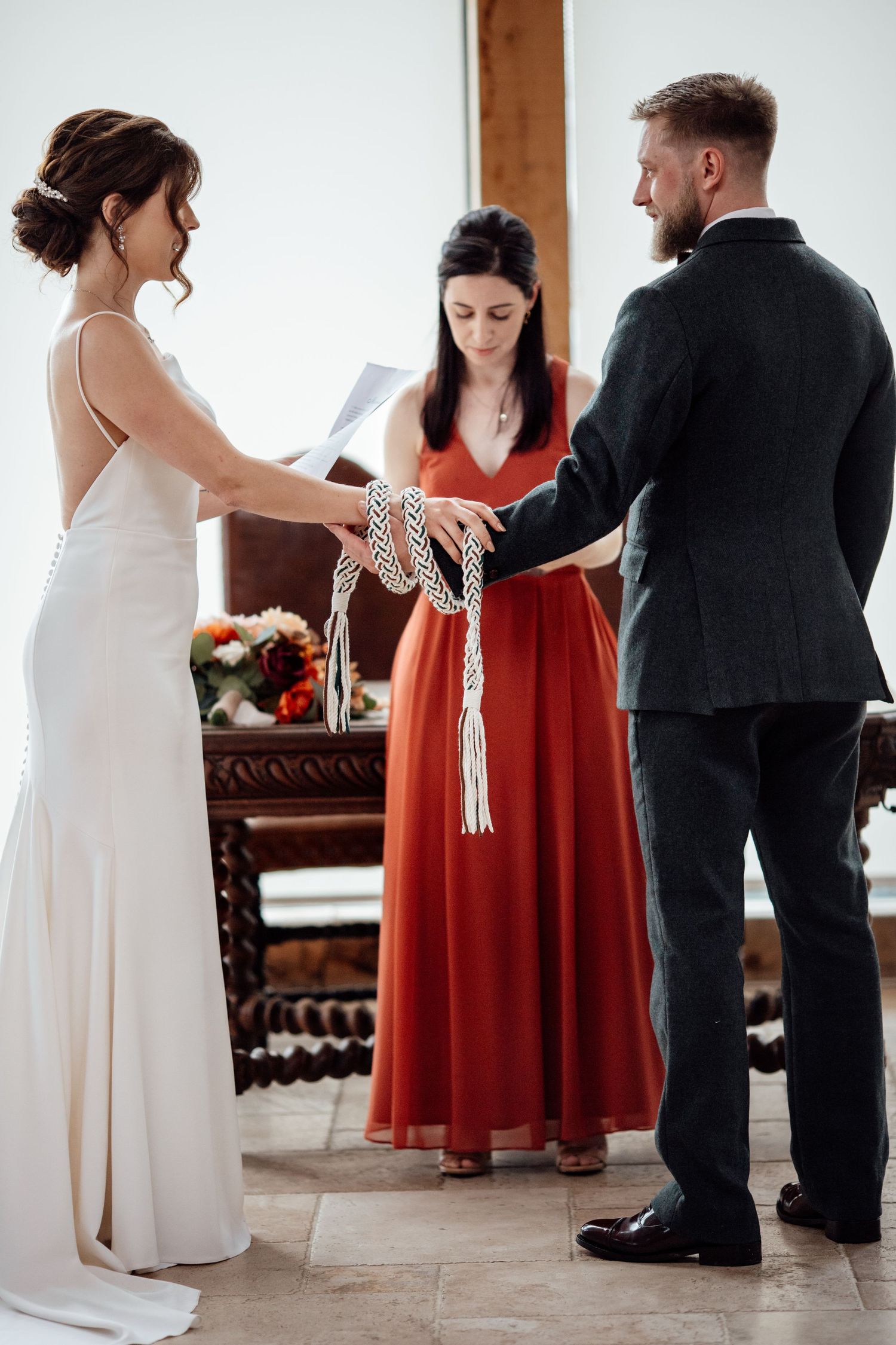 Wedding party members in red bridesmaid dresses and formal attire gather in an indoor venue.
