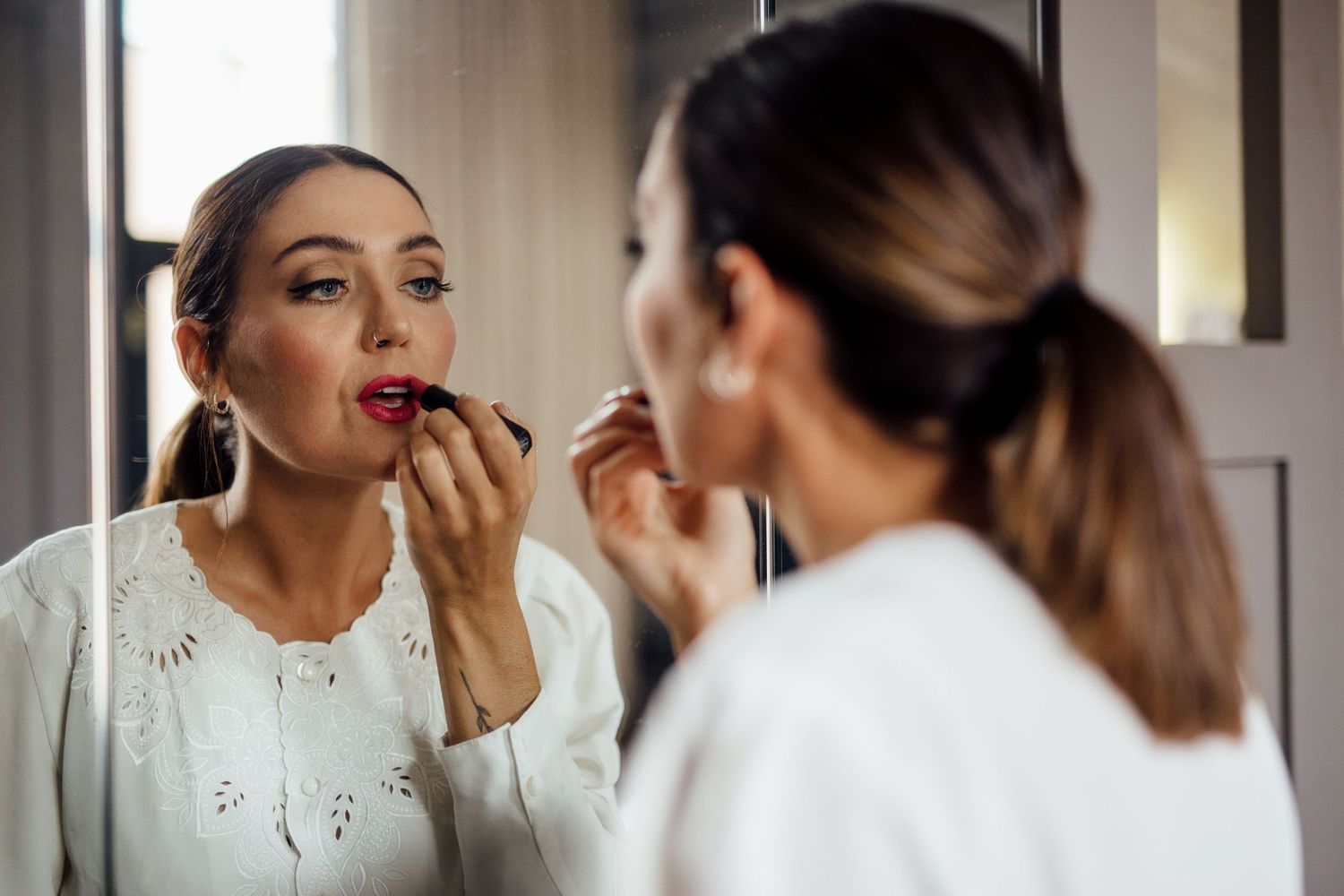 Reflection in mirror showing someone applying lipstick while getting ready.