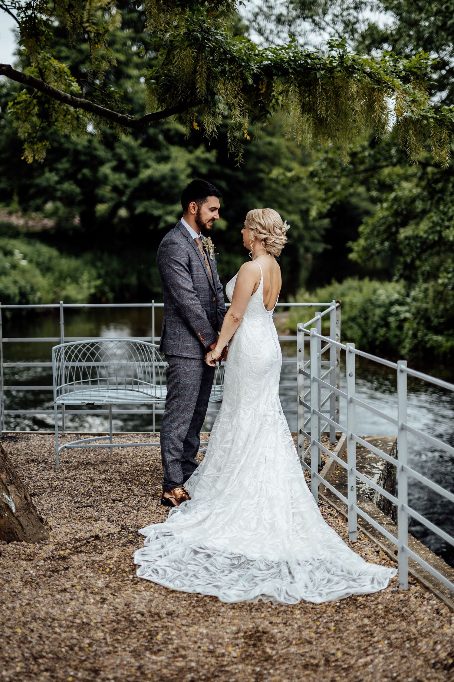 Wedding couple standing on rustic deck with metal railings surrounded by trees.