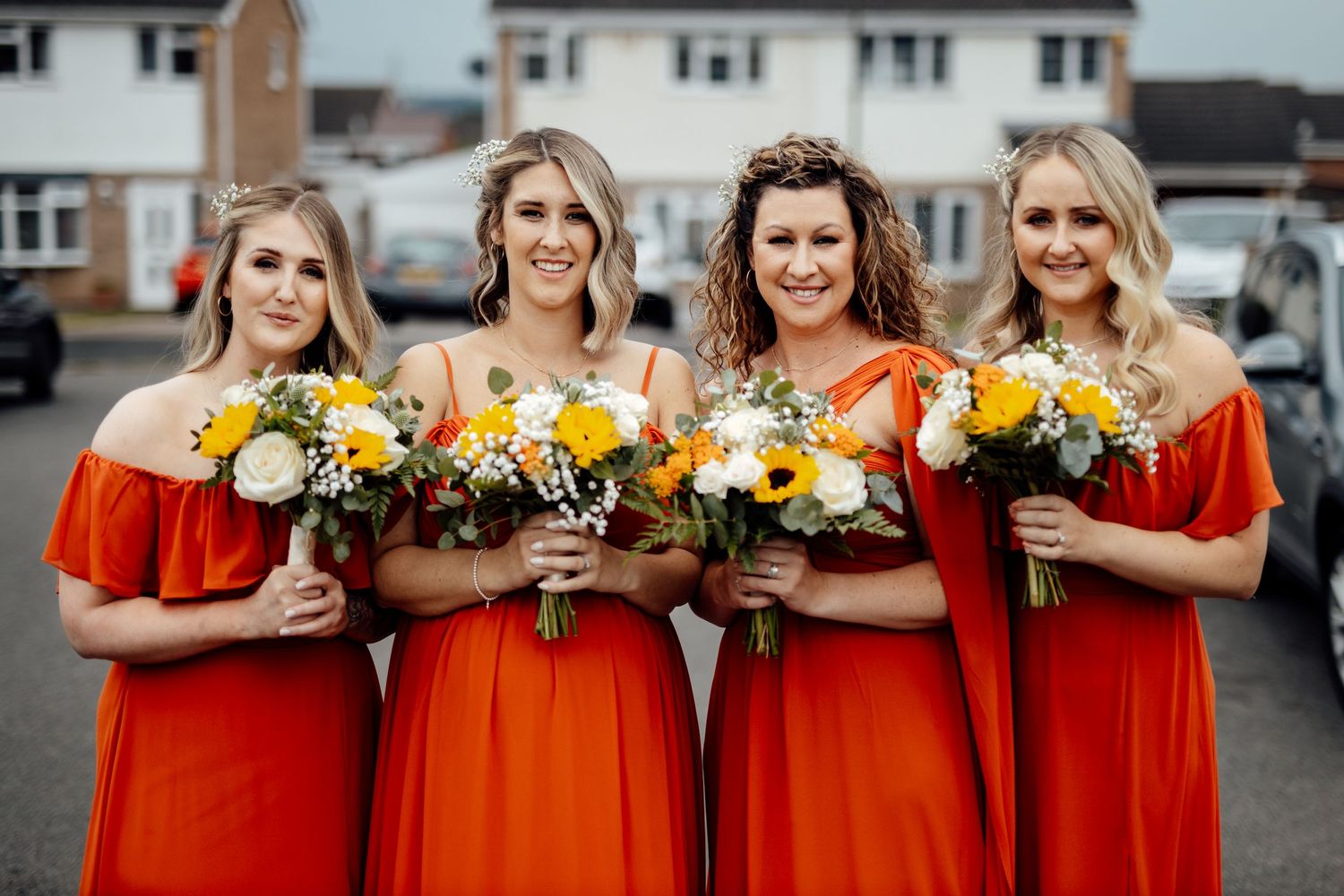 Wedding party members in red dresses pose together holding bouquets.