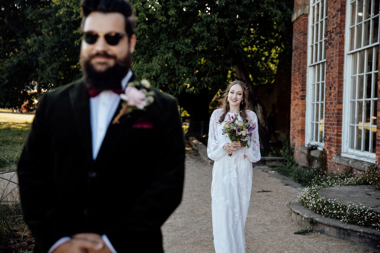 A wedding party walks together on a stone path surrounded by brick buildings and greenery.