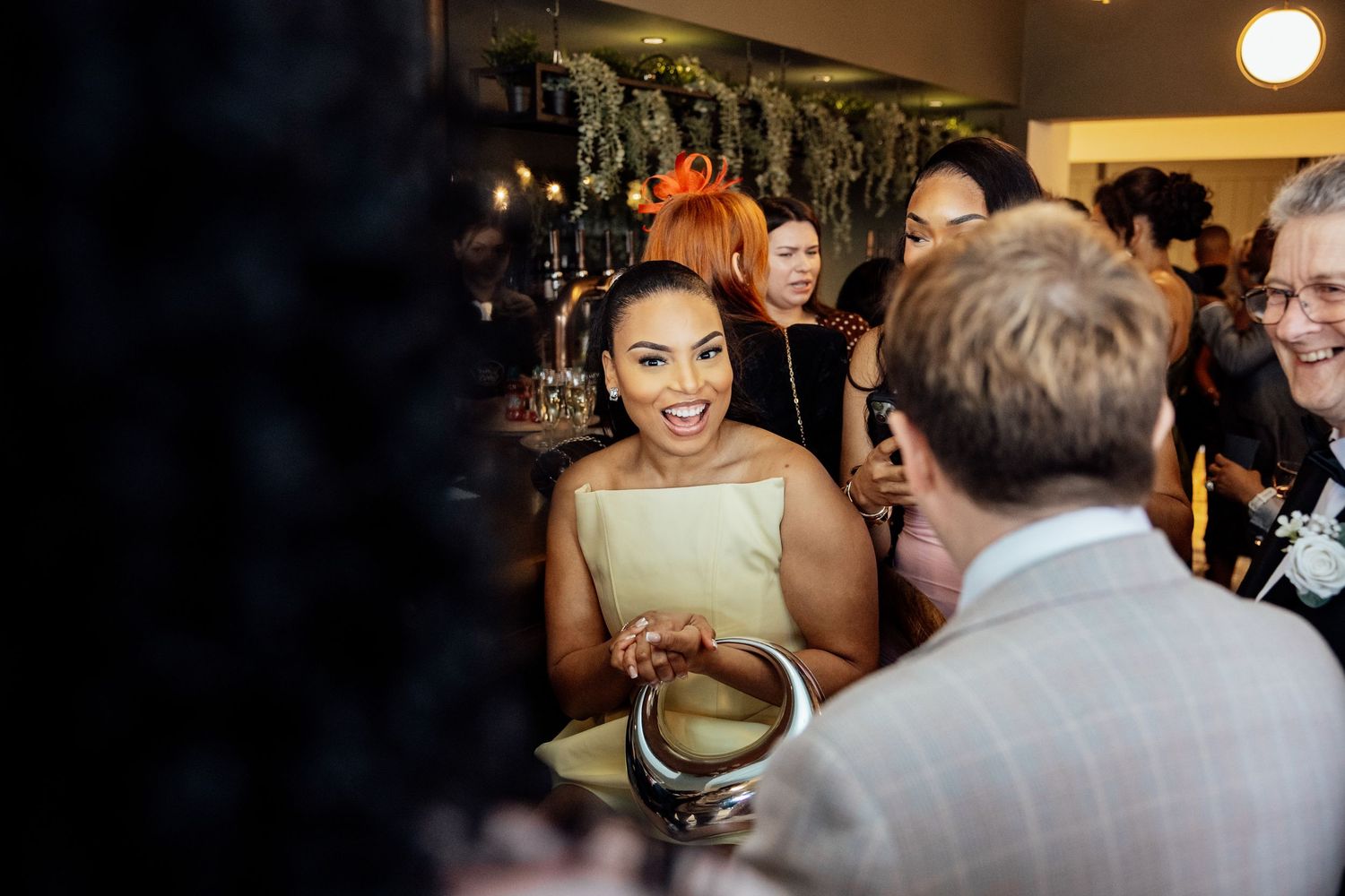 Wedding guest in gold dress laughing joyfully while socializing at elegant reception.