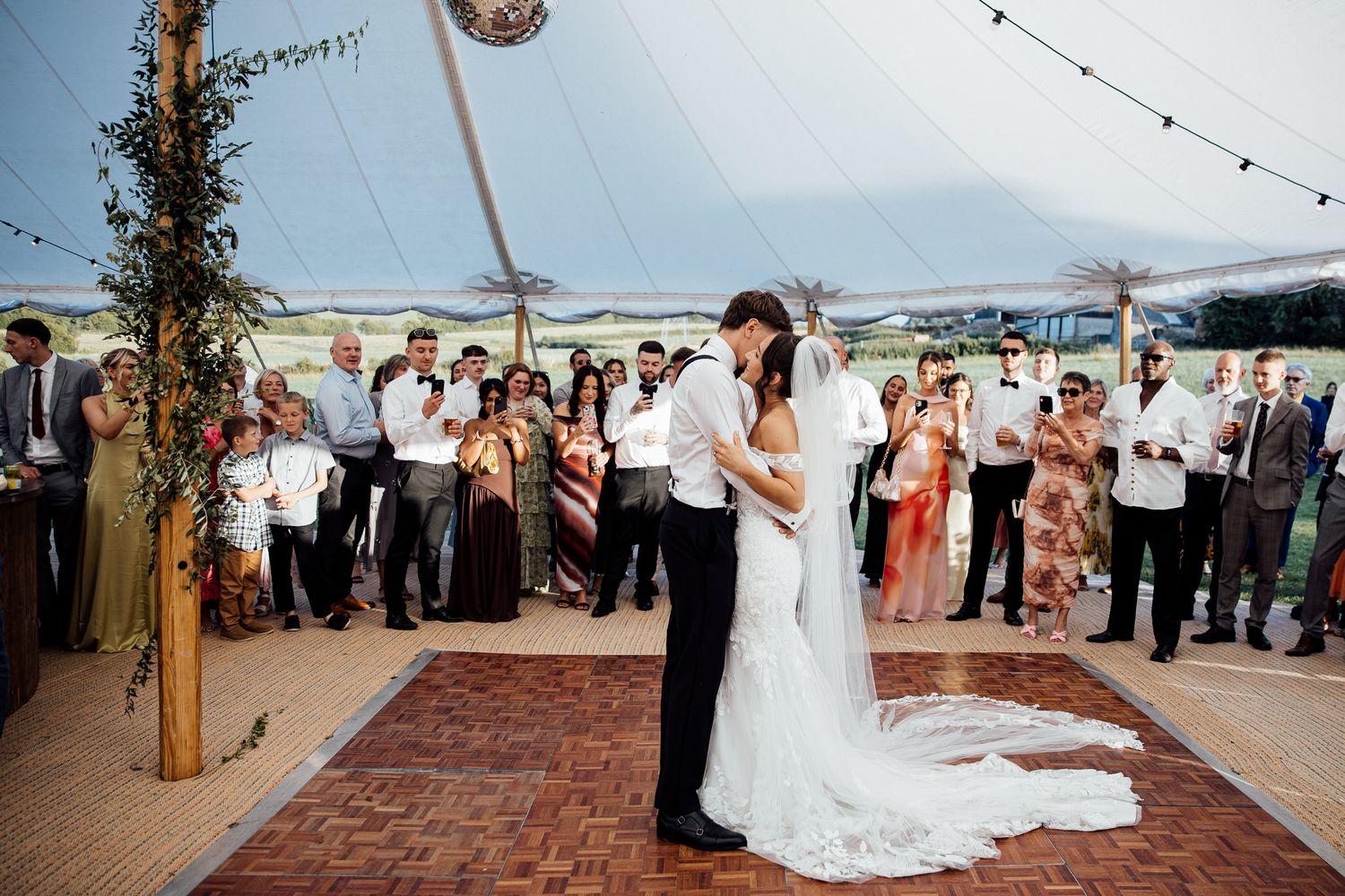 Outdoor wedding reception under string lights with guests dancing on wooden dance floor.