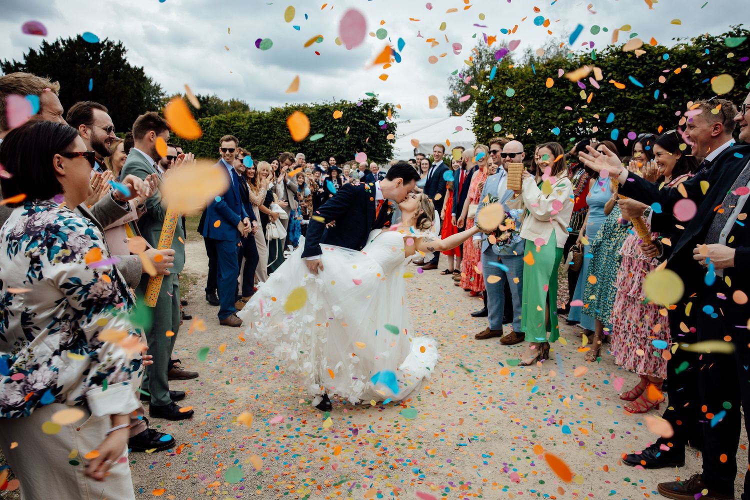 Wedding guests throw colorful confetti during a joyous outdoor celebration.