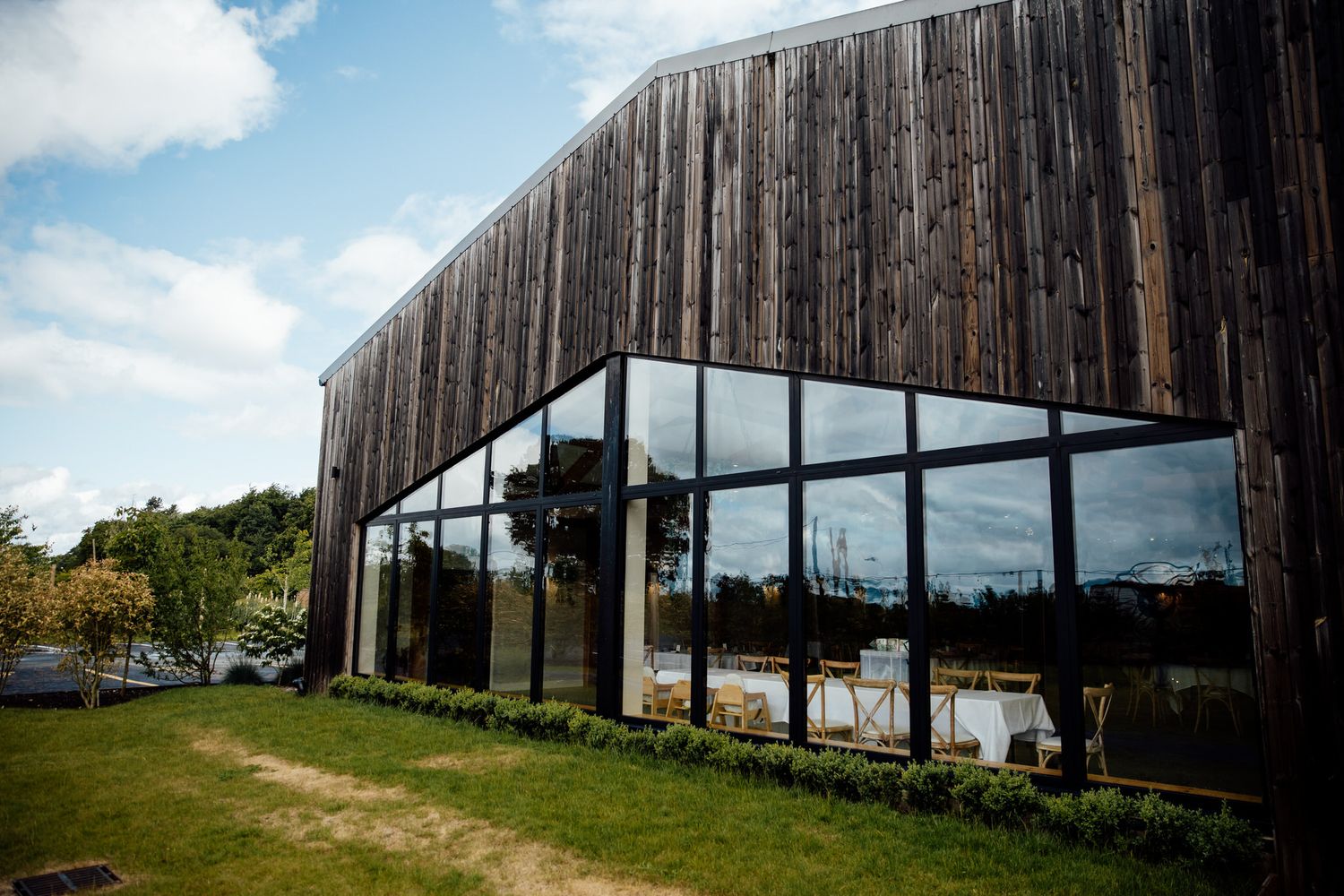 Long wooden barn exterior photographed against blue sky with clouds.