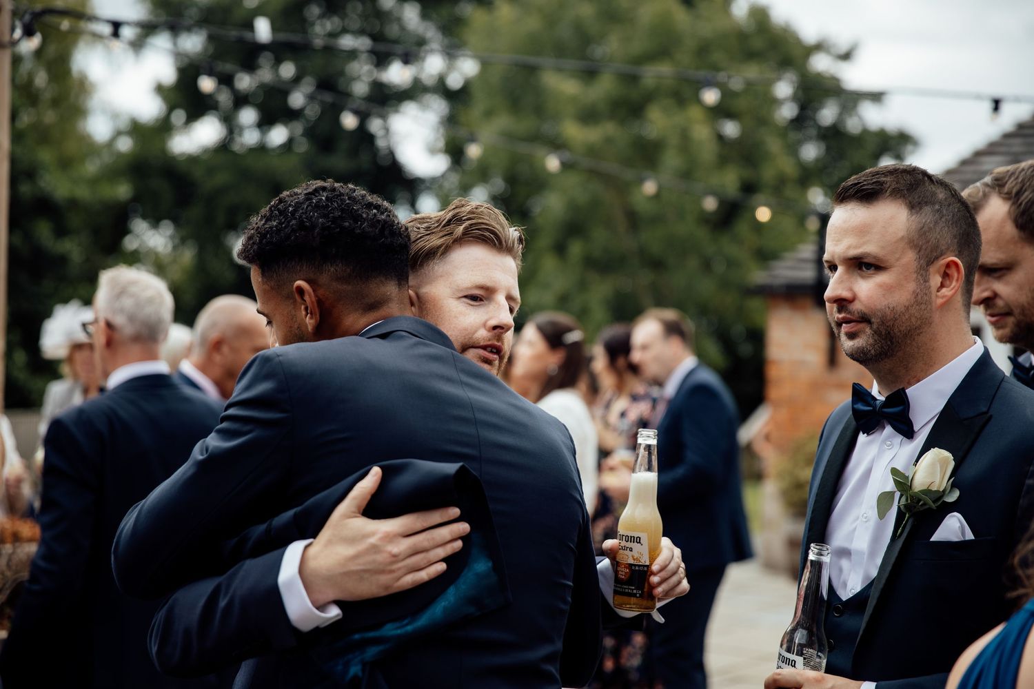 Wedding guests share emotional embraces during outdoor celebration.