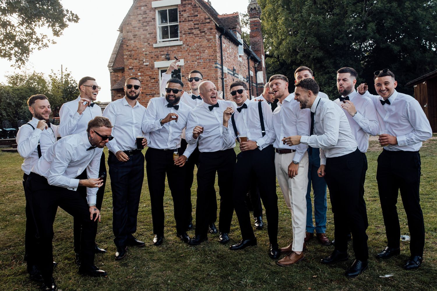 Groomsmen in white shirts and black ties pose together for a group photo outside a brick building.
