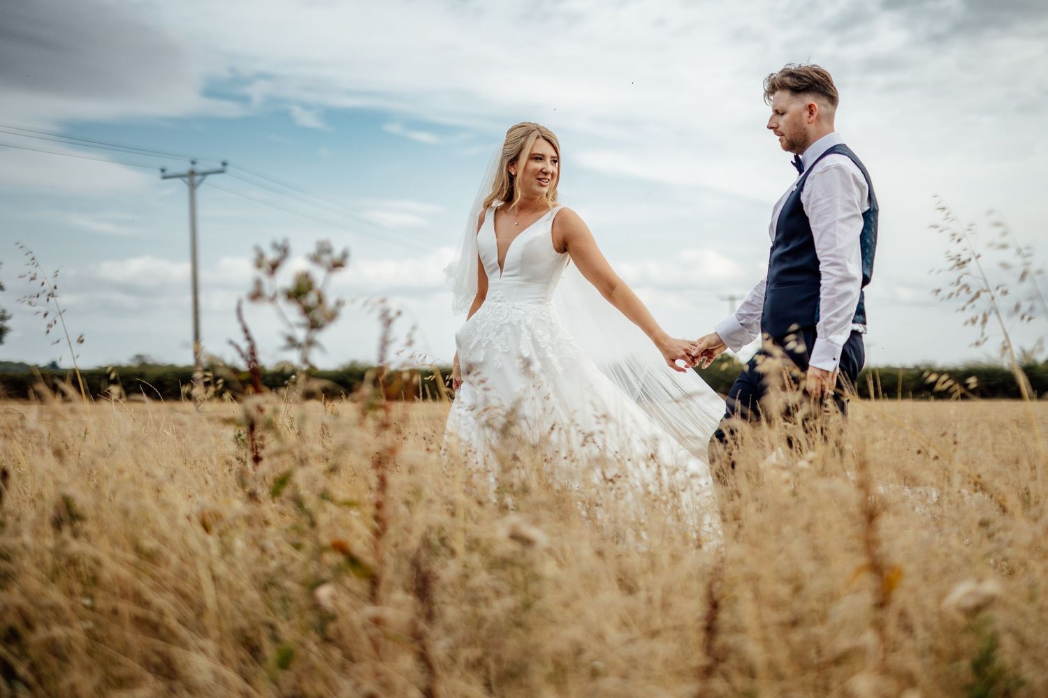 Romantic wedding photography session in golden wheat field under cloudy sky.