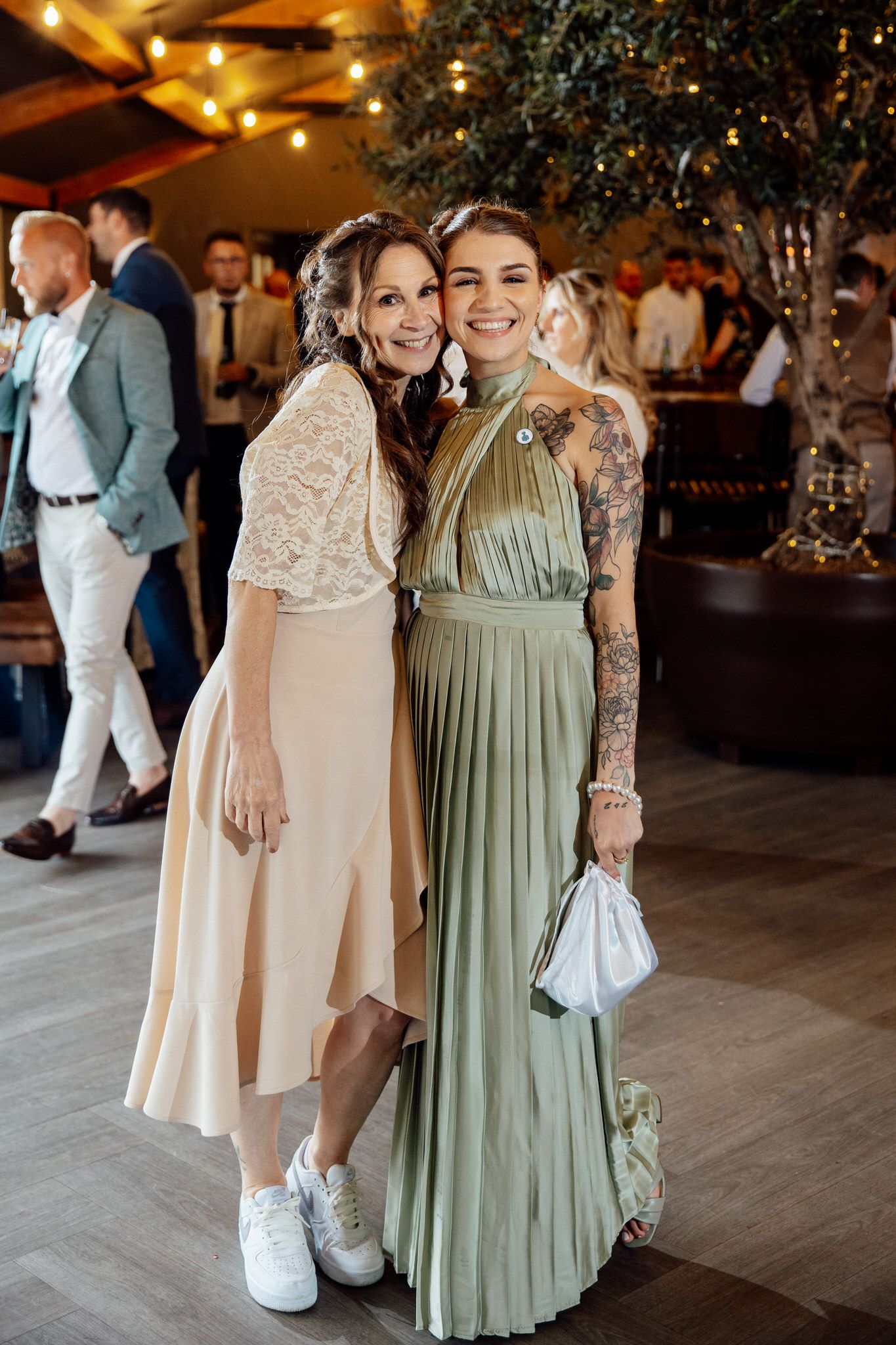 Wedding guests in sage green and cream dresses mingling on dance floor.