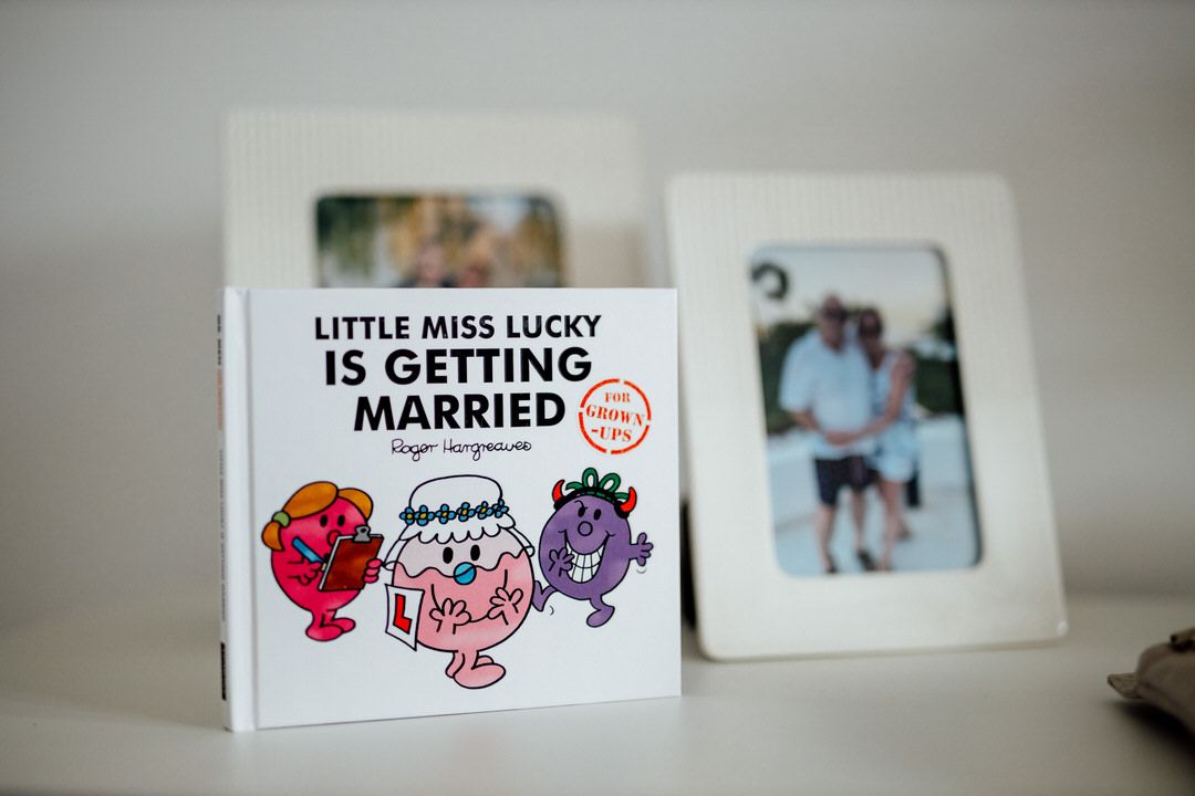Cute cartoon wedding card with text 'Little Miss Lucky is Getting Married' next to a framed photo.